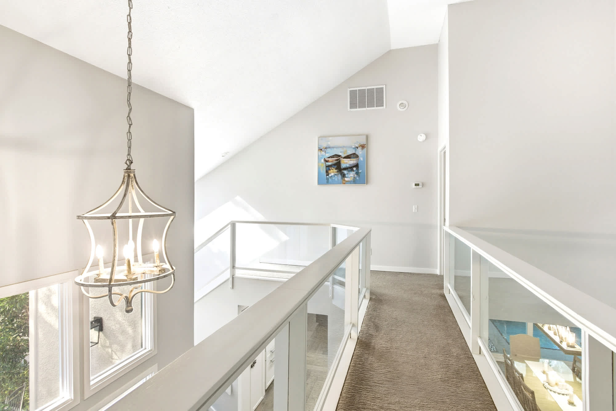 The upper hallway's statement gold chandelier, glass railing, and vaulted ceiling are as beautiful as they are functional.