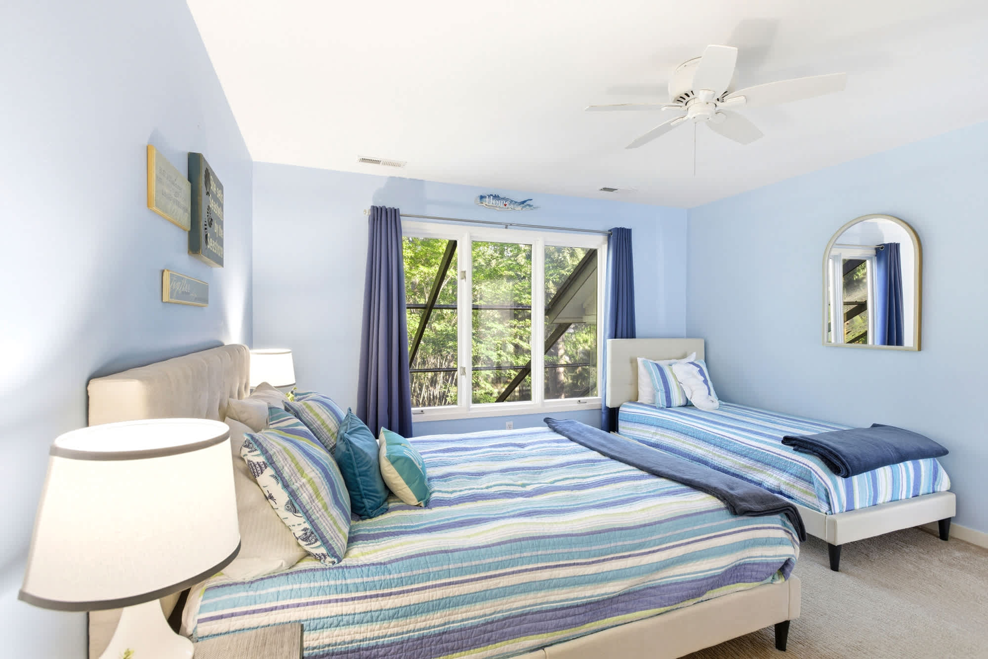 A queen and a twin share this sunny blue room, with a lush garden window view, a gold arch mirror, and nautical art accents.