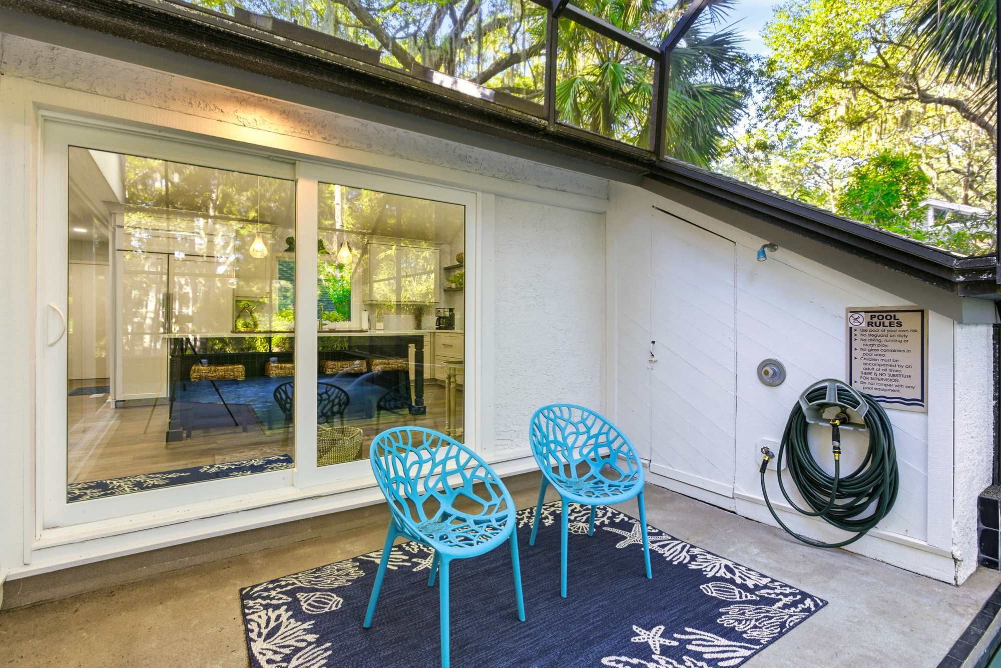 Teal lattice chairs on a coral-print outdoor rug welcome you at the pool patio, with sliding glass doors connecting directly to the bedroom and pool area.