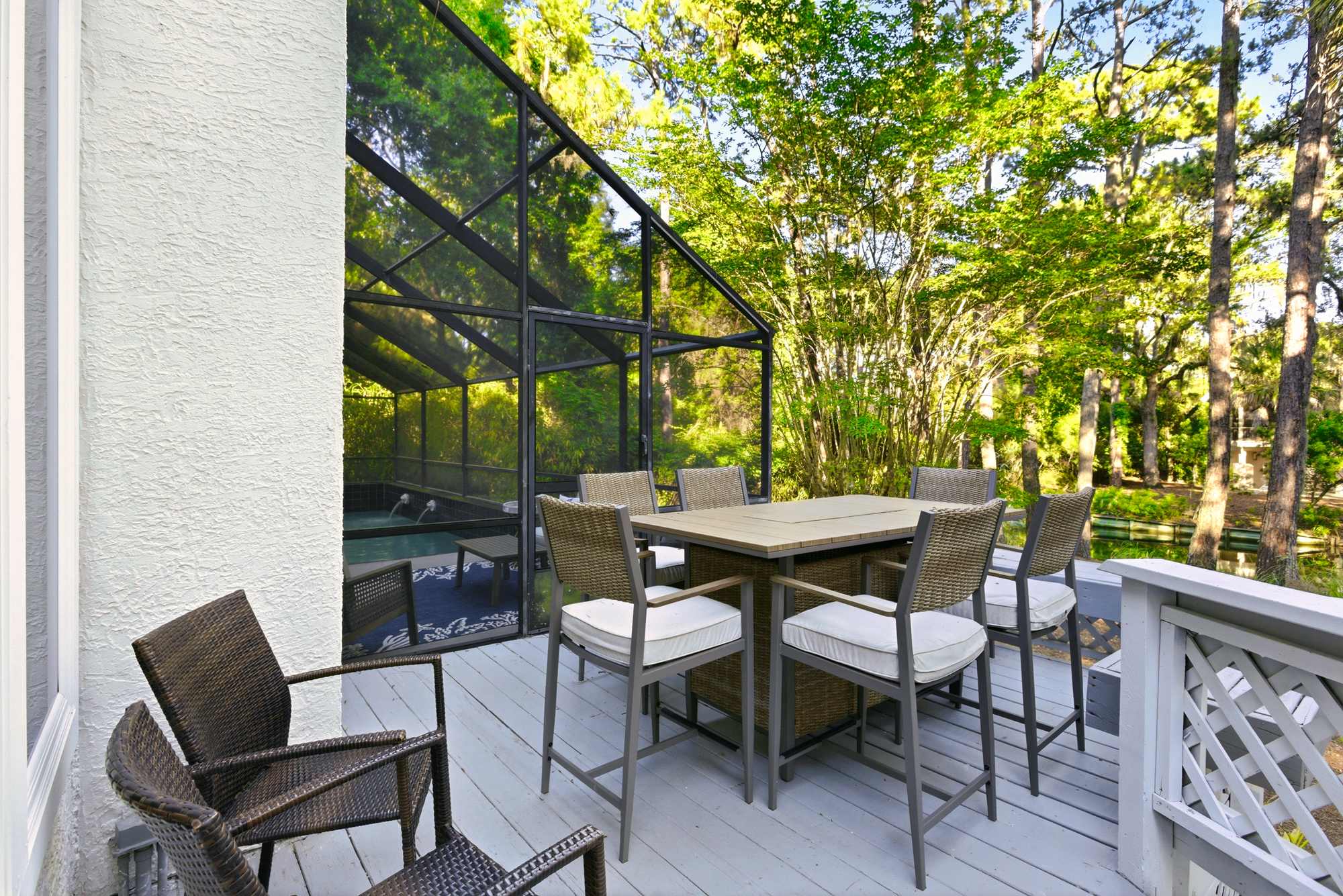 An upper-level deck with a wicker dining set for six overlooks the screened pool enclosure and the private, tree-filled backyard.