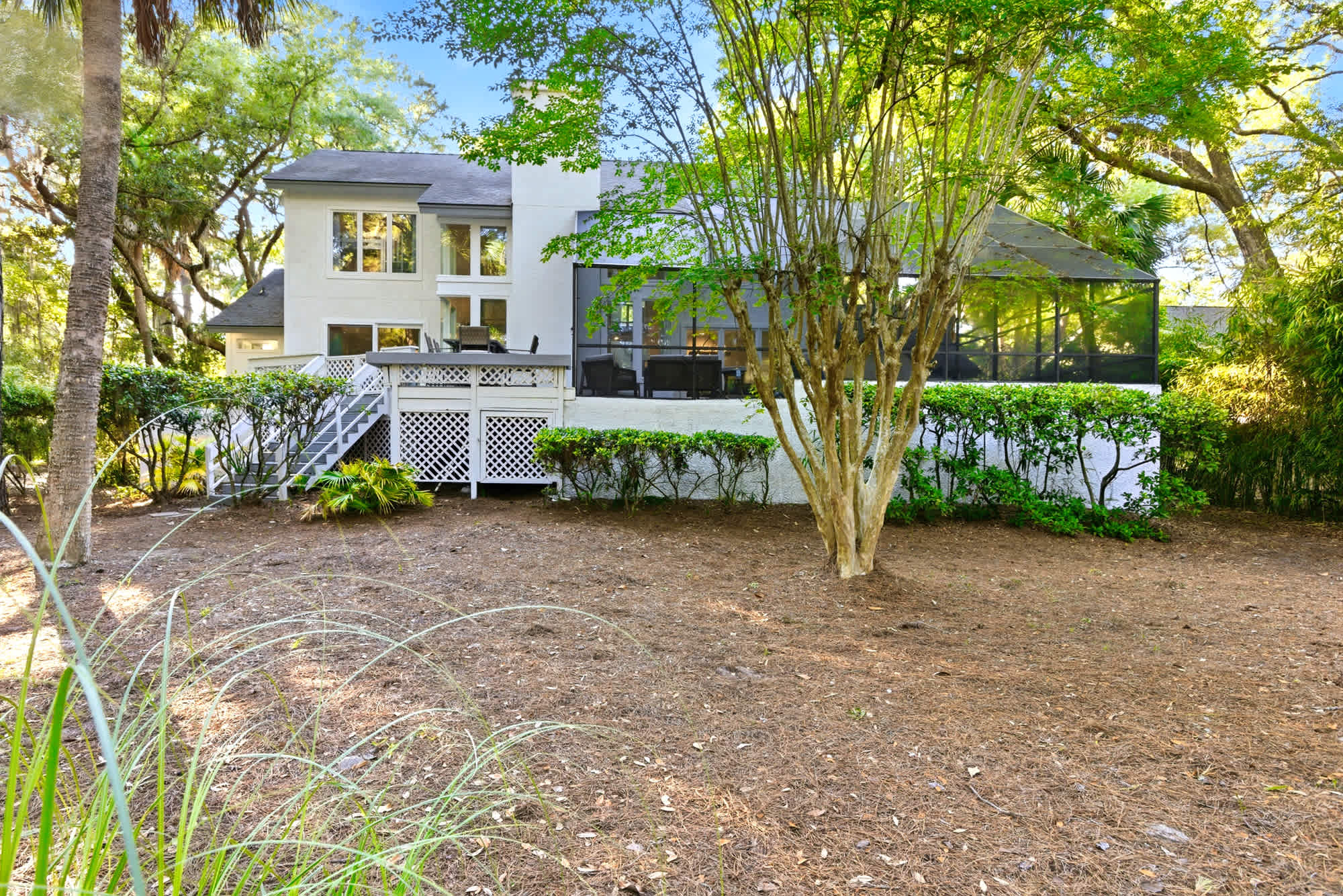 The full rear facade showcases the white exterior, lattice-railed decks, staircase, screened enclosure, and natural bamboo and oak surroundings.