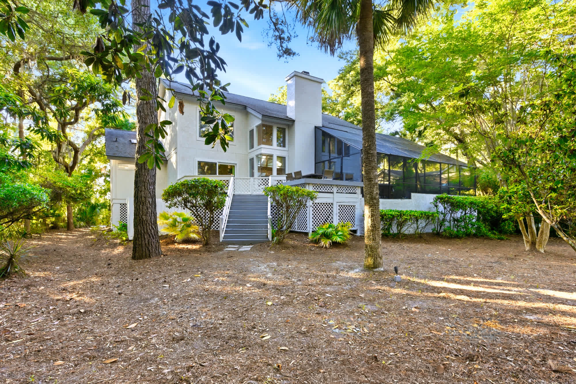 Draped in live oaks and palms, the two-story white home with its stacked chimney and multi-level decks makes a striking impression from the backyard.