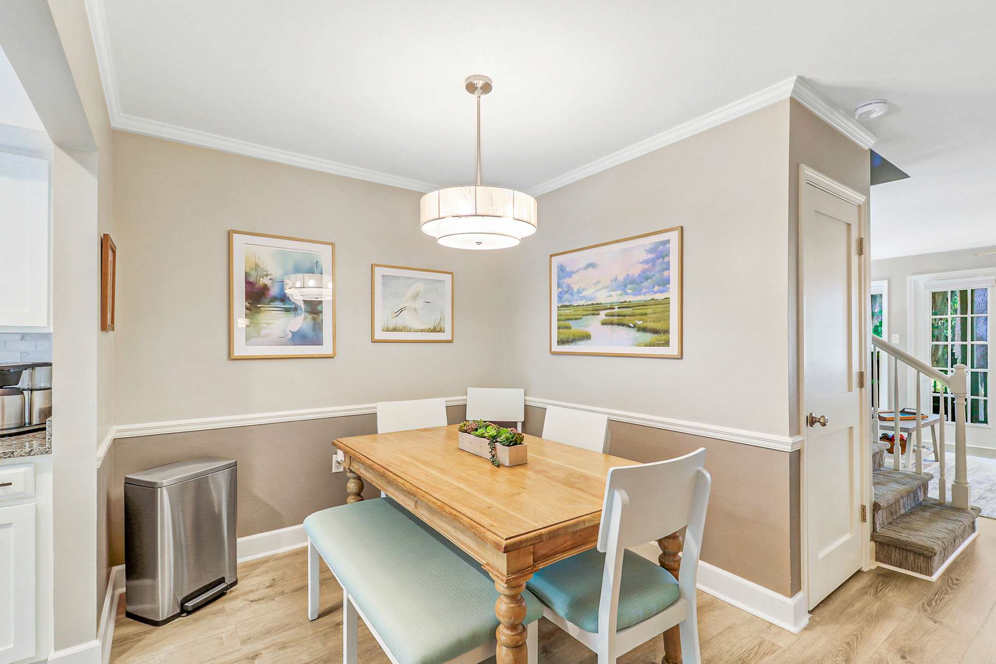 The dining area offers plenty of room for group dinners and game nights. Coastal marsh watercolors and two-tone walls create a relaxed, upscale feel guests love.