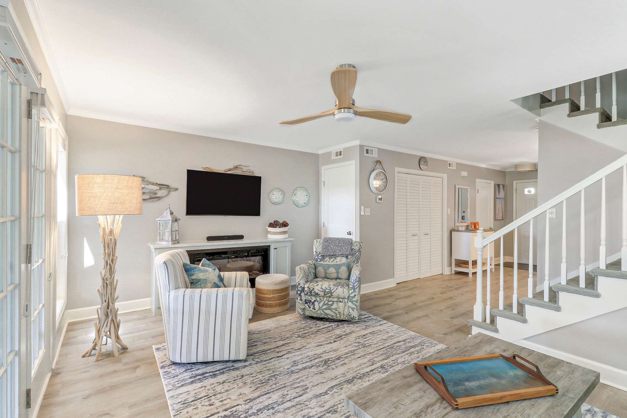 Spacious, light-filled living room with room for the whole group to gather. Features a TV/fireplace wall, multiple seating areas, deck access, and easy staircase access to upper bedrooms.