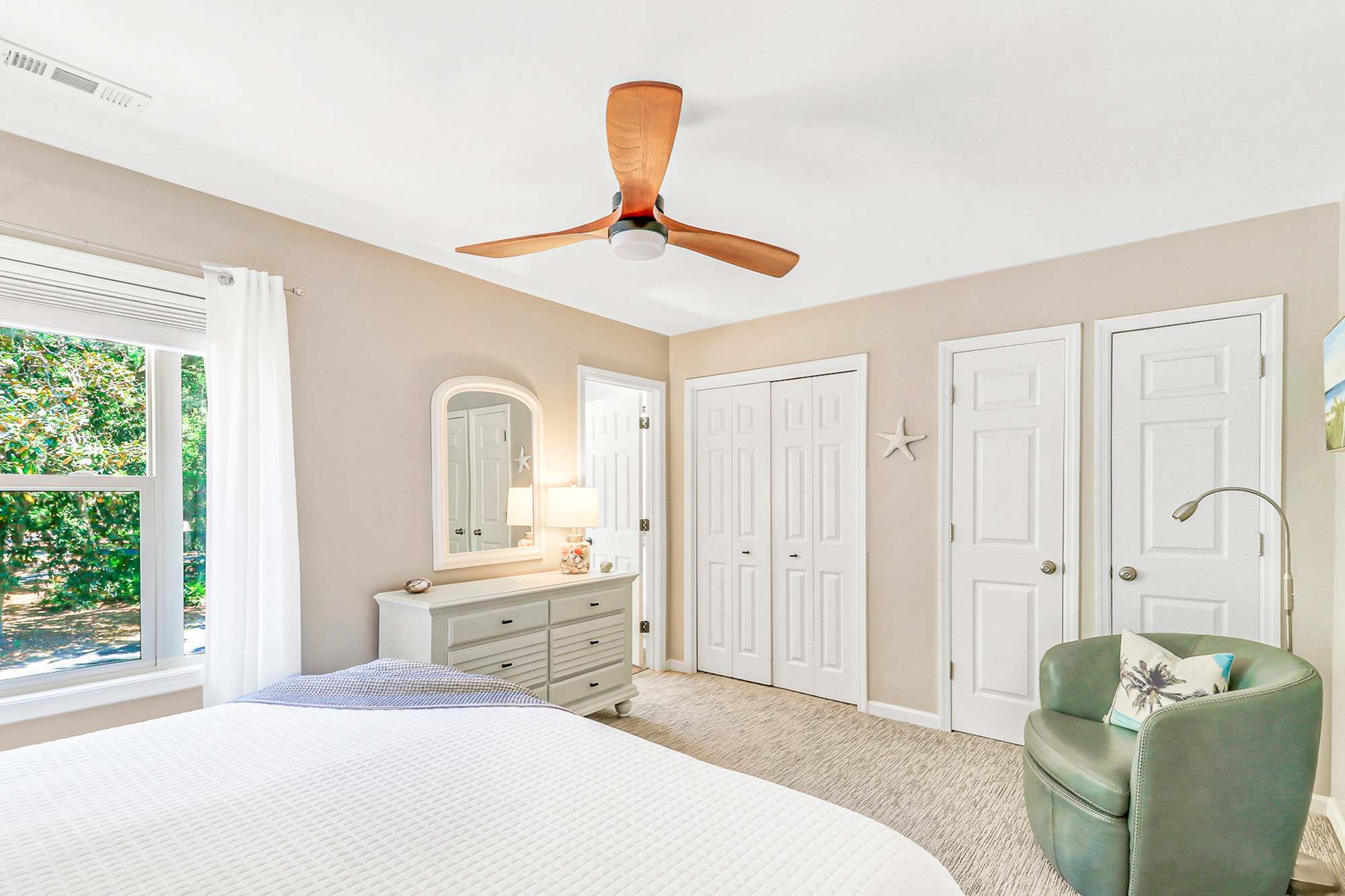 Rest easy in the generous primary bedroom with a king bed, dual closets, and a large window. A seafoam accent chair and dresser with mirror complete this private, comfortable retreat.