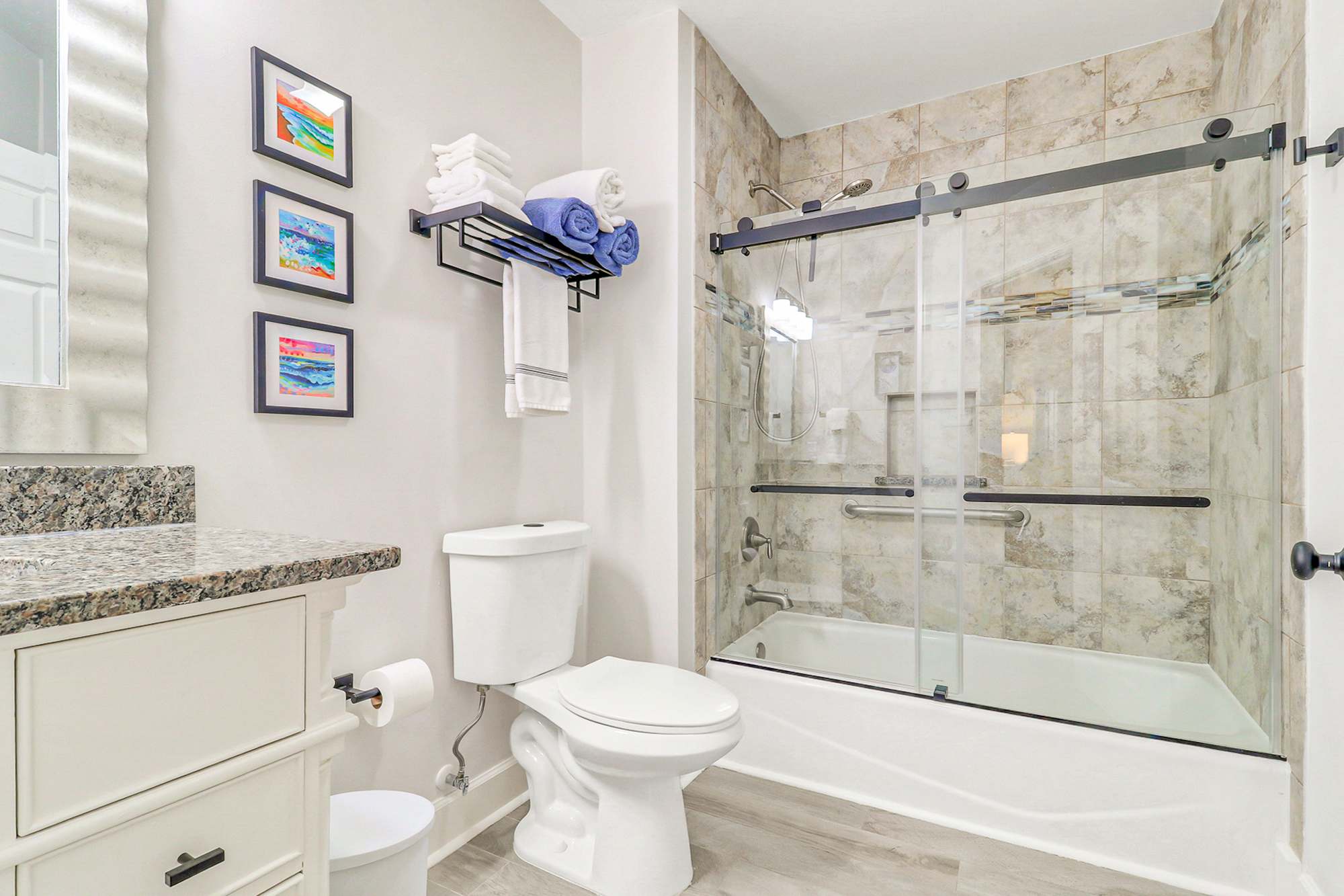 Second full bath with a tub/shower combo, frameless glass door, and stone tile surround. Great for families or guests who prefer a soak. Fresh towels and coastal art included.