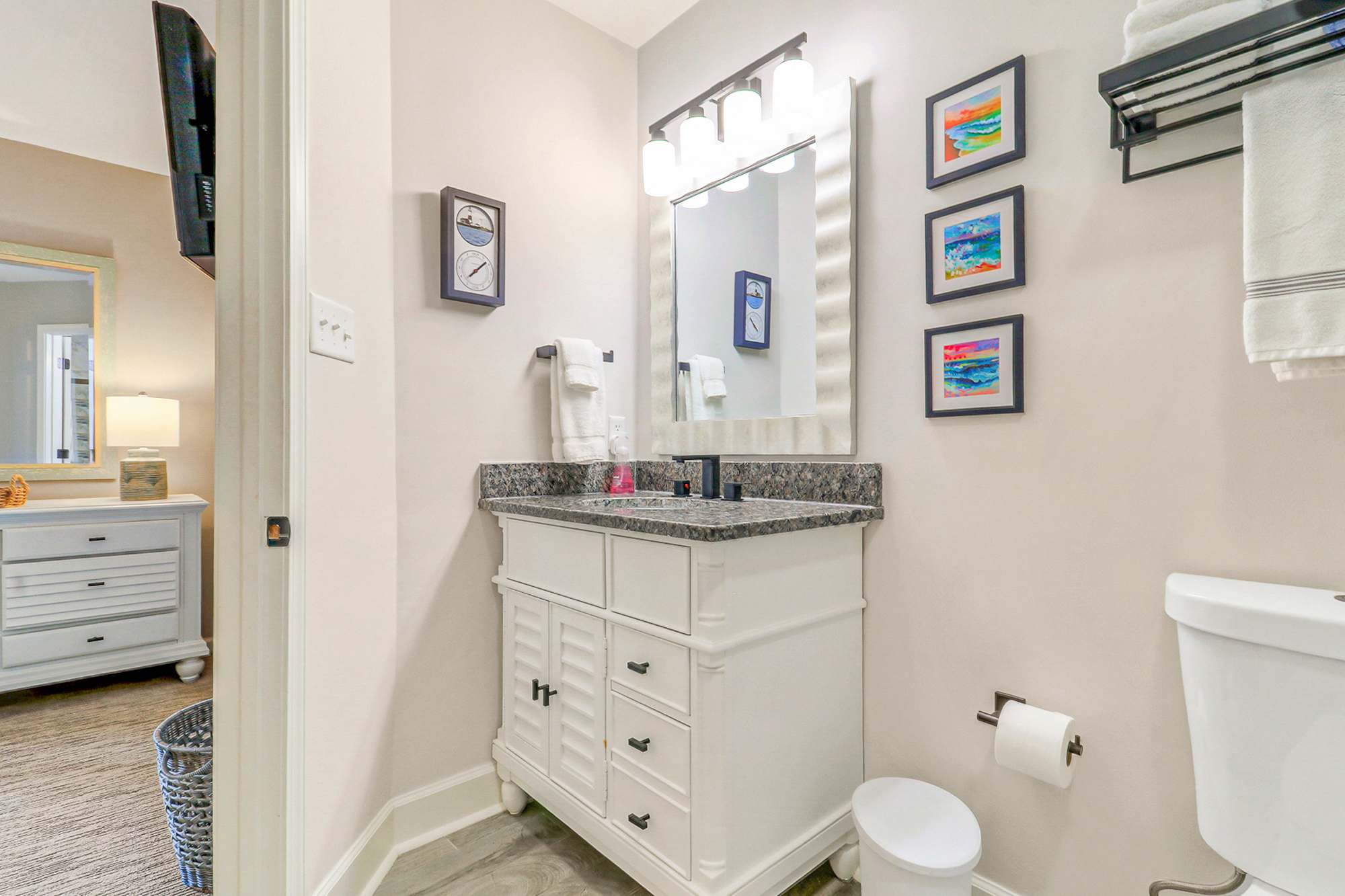 Well-appointed second bathroom vanity with granite top, lighted mirror, and vibrant coastal art. Conveniently connected to the second bedroom for easy access during your stay.