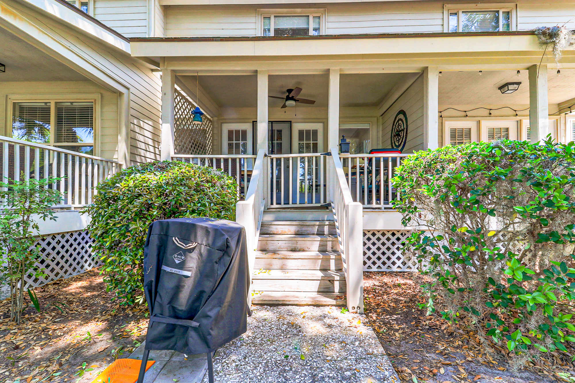 A classic coastal cottage exterior framed by mature shrubs and a shaded covered porch. Steps lead up to the welcoming entry, giving guests a true Lowcountry arrival experience.