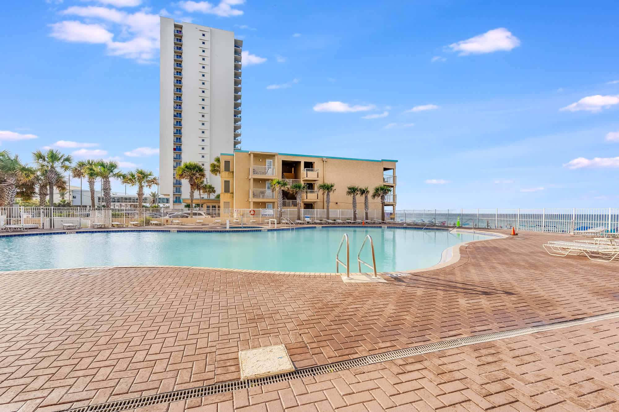 Tidewater 200 – Outdoor pool with lounge chairs and palm trees, surrounded by a building and ocean view.
