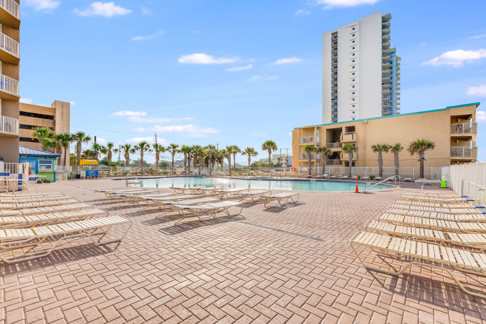 Tidewater 200 – Outdoor pool area with lounge chairs and palm trees, alongside a three-story vacation rental building.