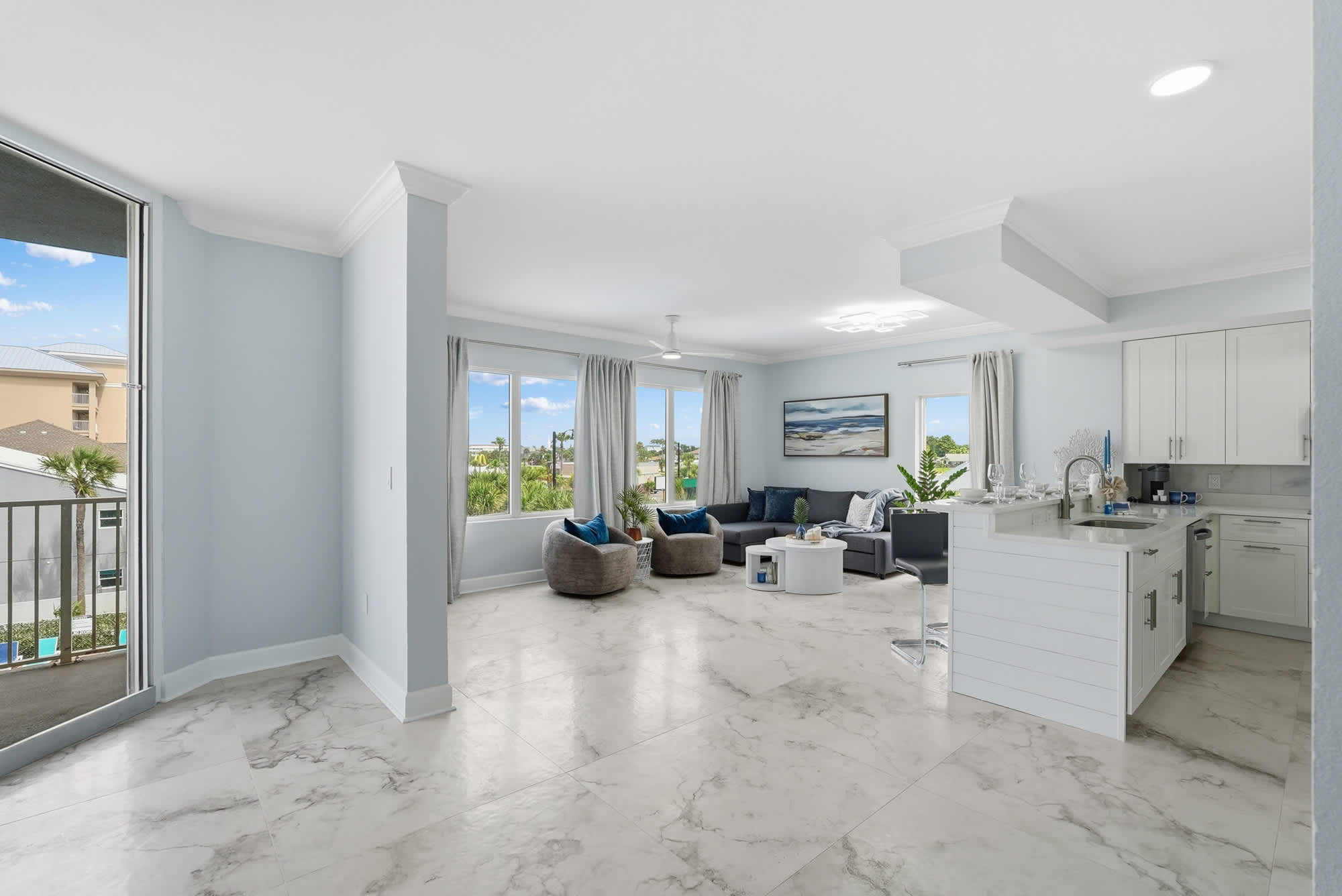 Tidewater 200 – Bright living area with modern furniture, large windows, and a kitchen counter. Outdoor view includes palm trees.