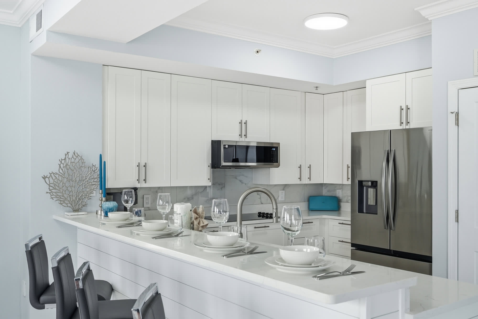 Tidewater 200 – Modern kitchen with white cabinets, stainless steel appliances, and a bar with gray stools and tableware.