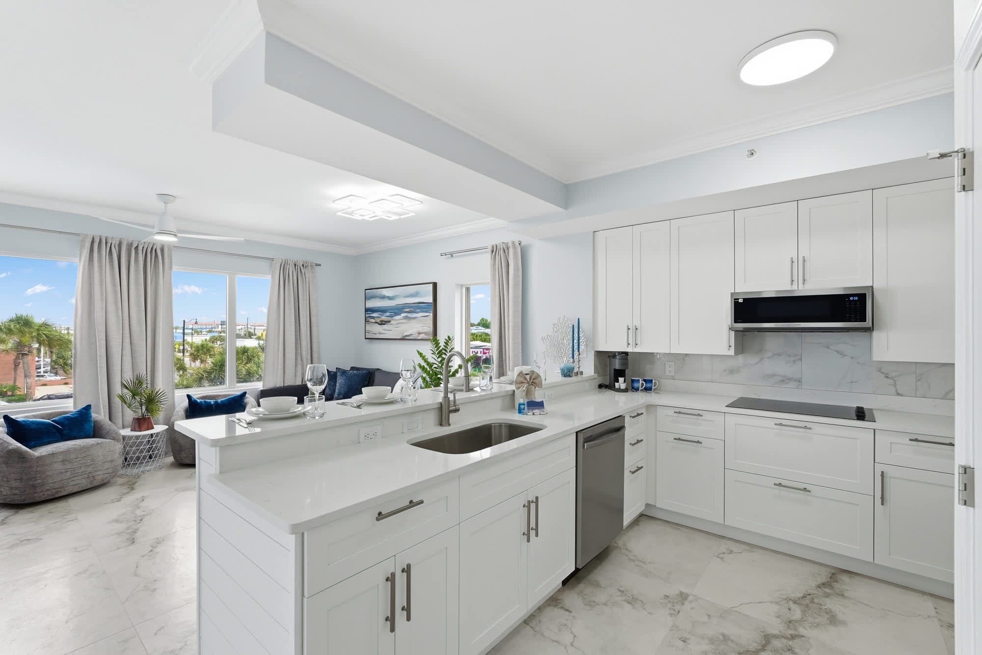 Tidewater 200 – Modern kitchen with marble countertops, adjacent living area, large windows, and views of palm trees.