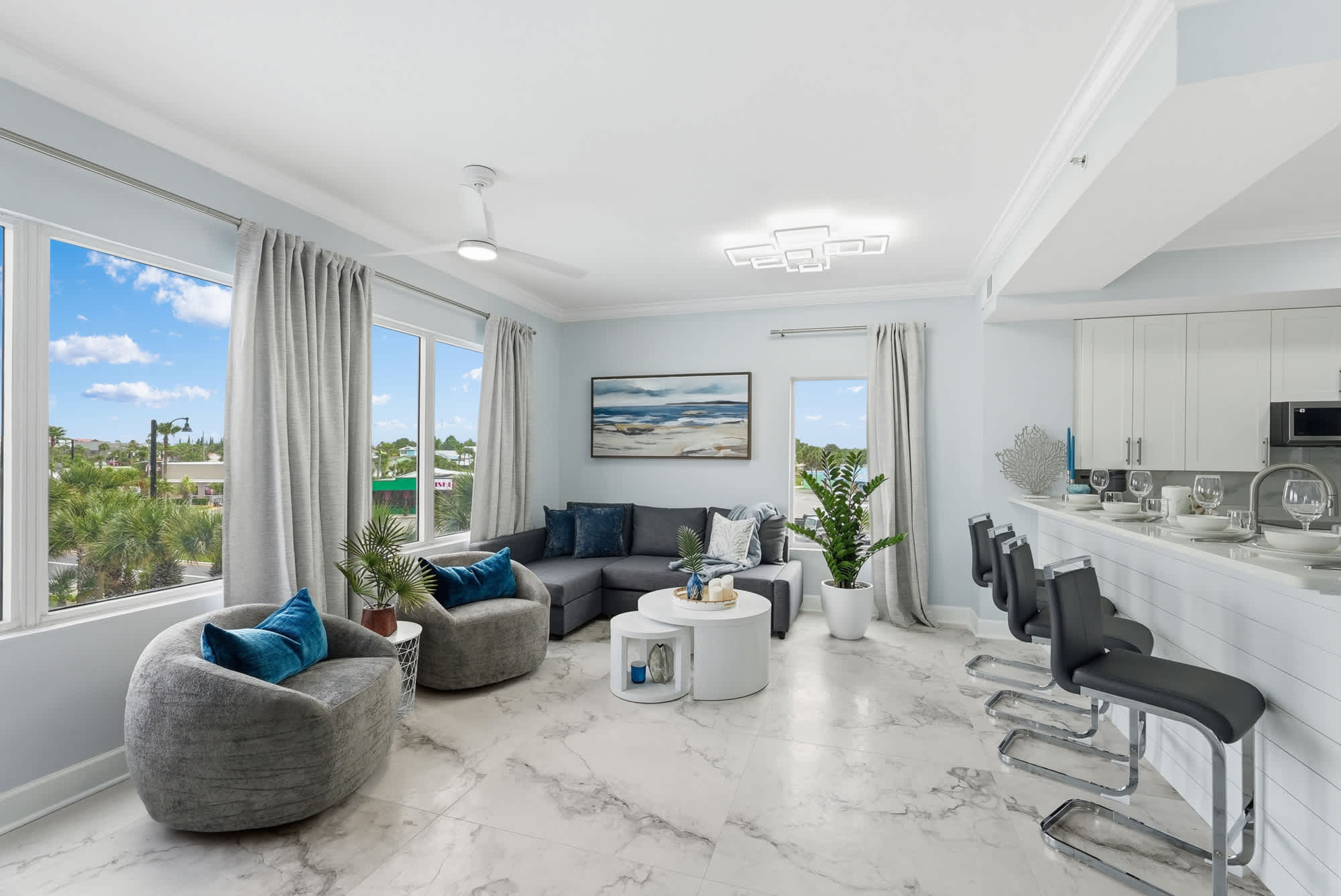 Tidewater 200 – Bright living room with large windows, gray sectional sofa, two cozy chairs, and a modern kitchen bar.