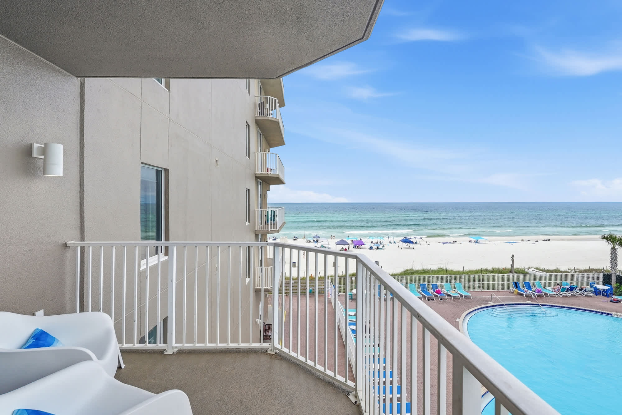 Tidewater 200 – Balcony view with white chairs, overlooking pool and beach with umbrellas and ocean in the background.
