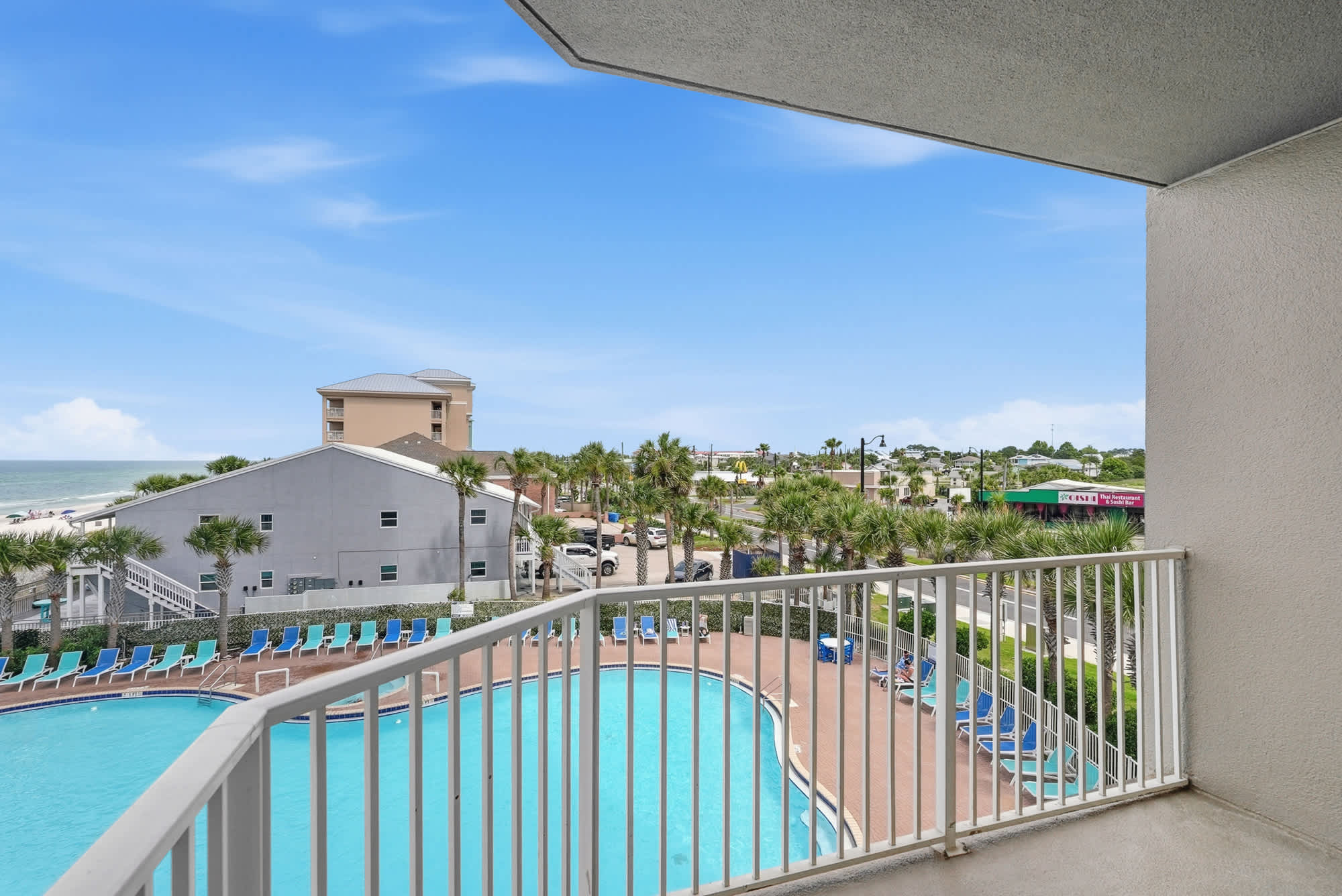 Tidewater 200 – Balcony view of outdoor pool area and surrounding palm trees, with ocean in the distance.