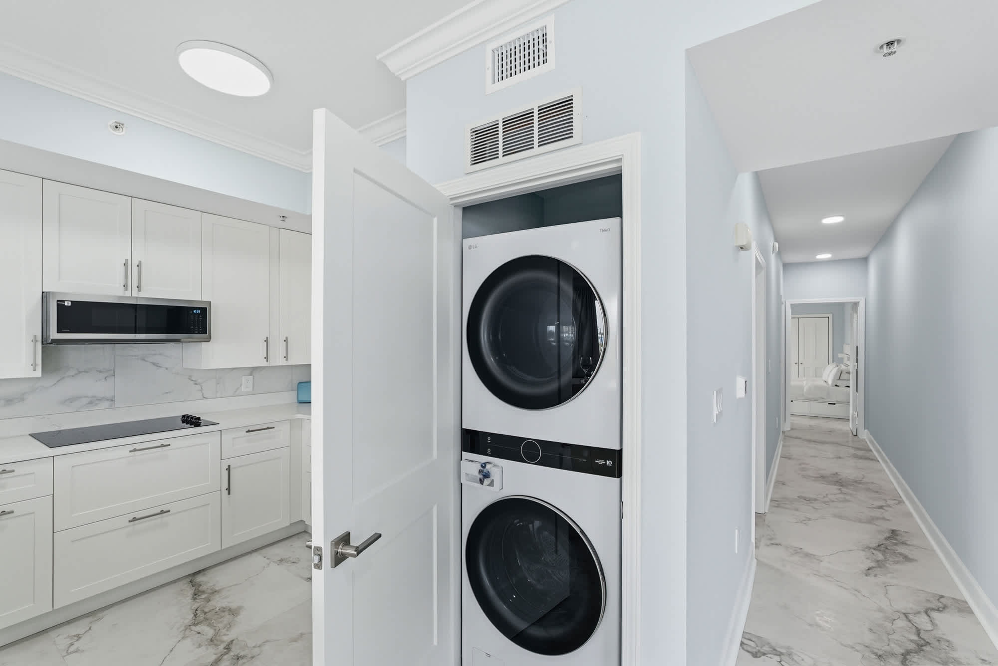 Tidewater 200 – Modern kitchen area with white cabinets, stacked washer and dryer, and a marble floor in the hallway.