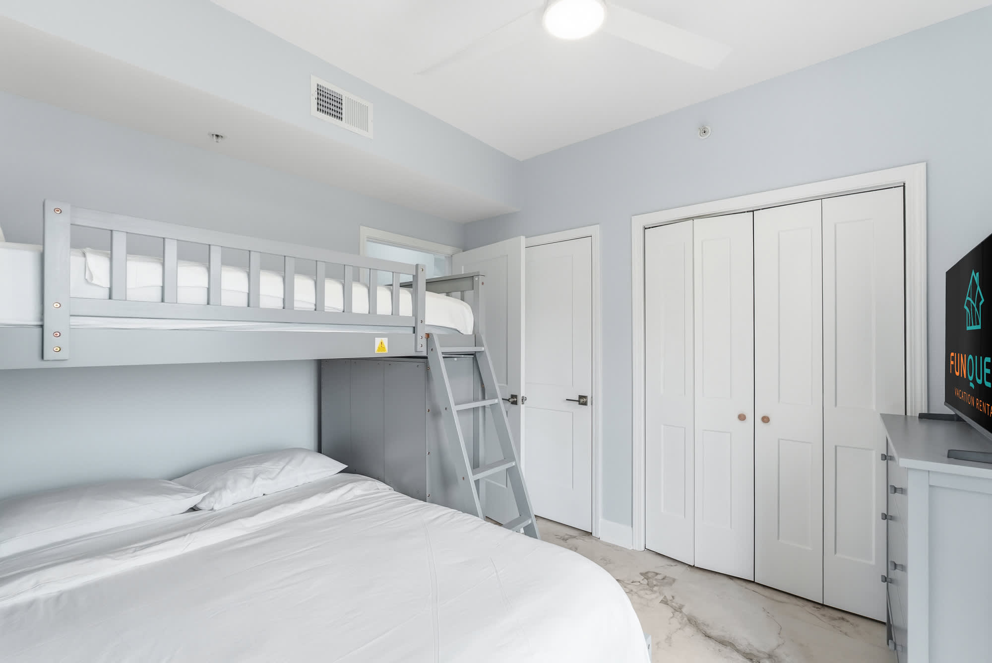 Tidewater 200 – Bedroom with a bunk bed, queen bed, and closet storage. Light gray walls and a television.