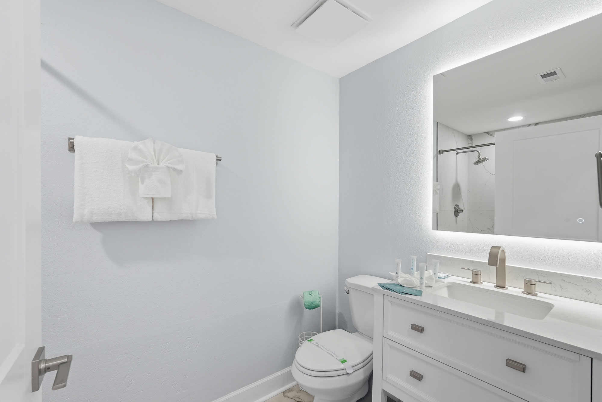 Tidewater 200 – Bright bathroom with light blue walls, a shower, modern sink, white towels, and a illuminated mirror.