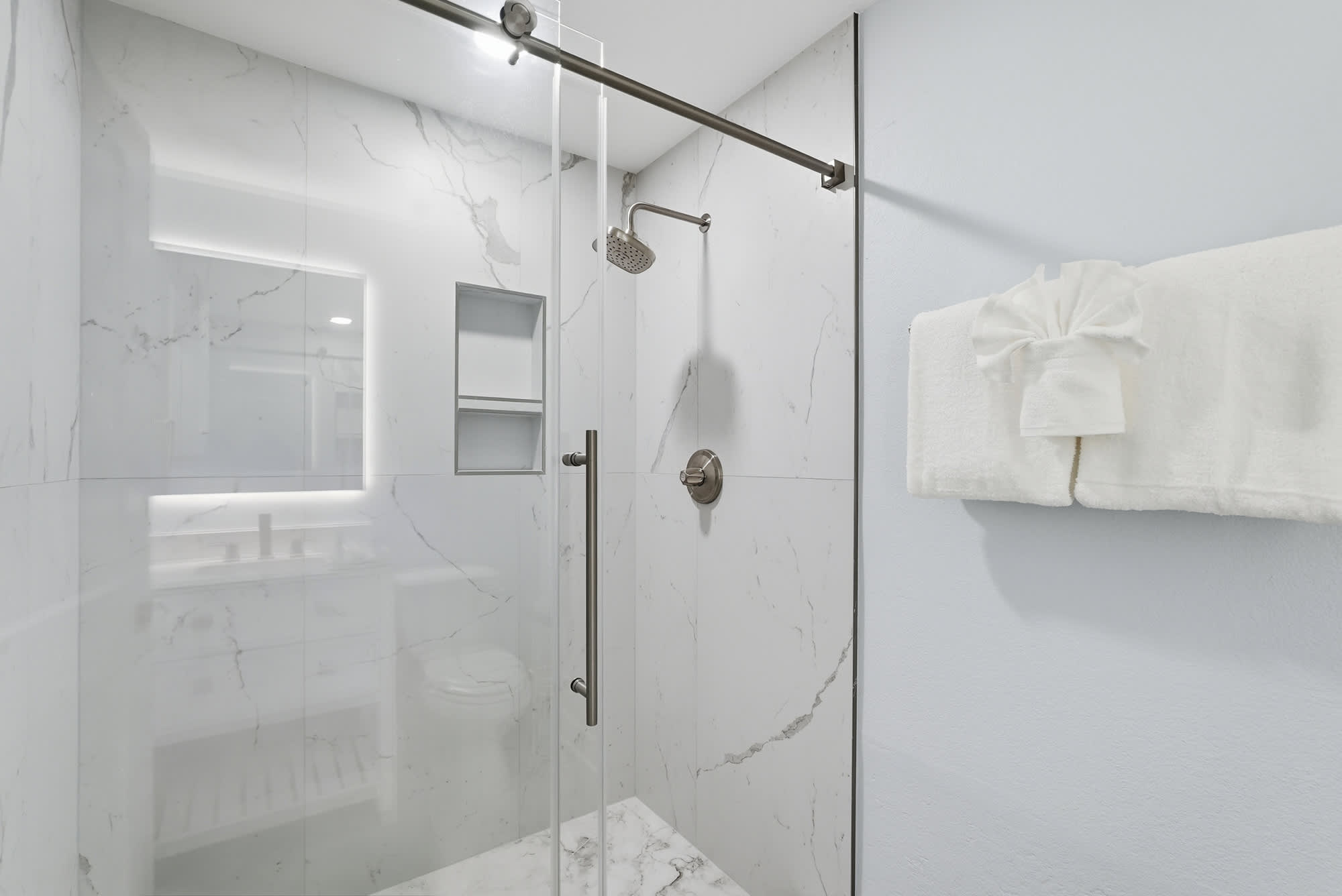 Tidewater 200 – Modern bathroom with glass shower, white marble walls, and a neatly folded towel on a rack.