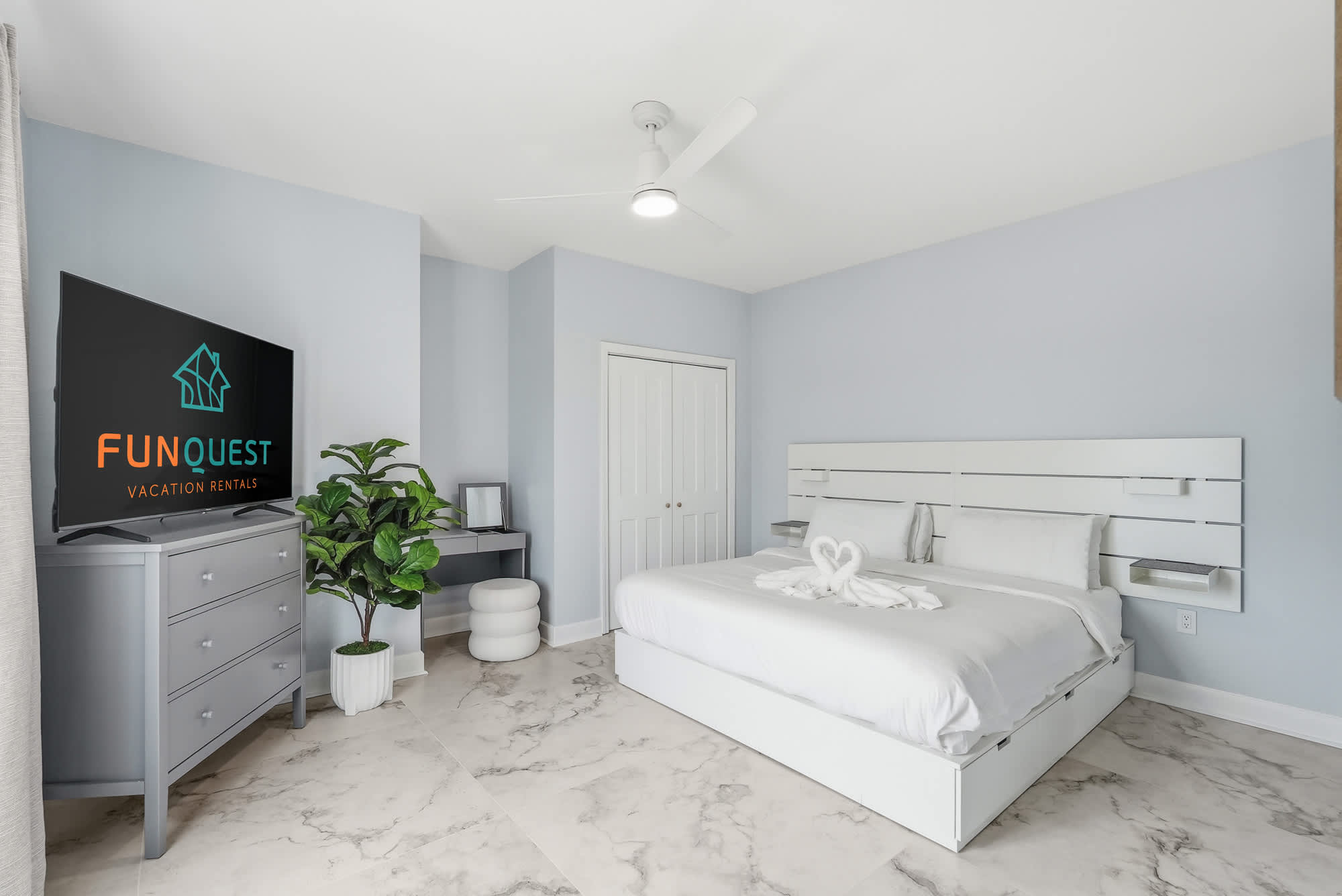 Tidewater 200 – Modern bedroom with a king-sized bed, television, desk, plant, and light-colored marble flooring.