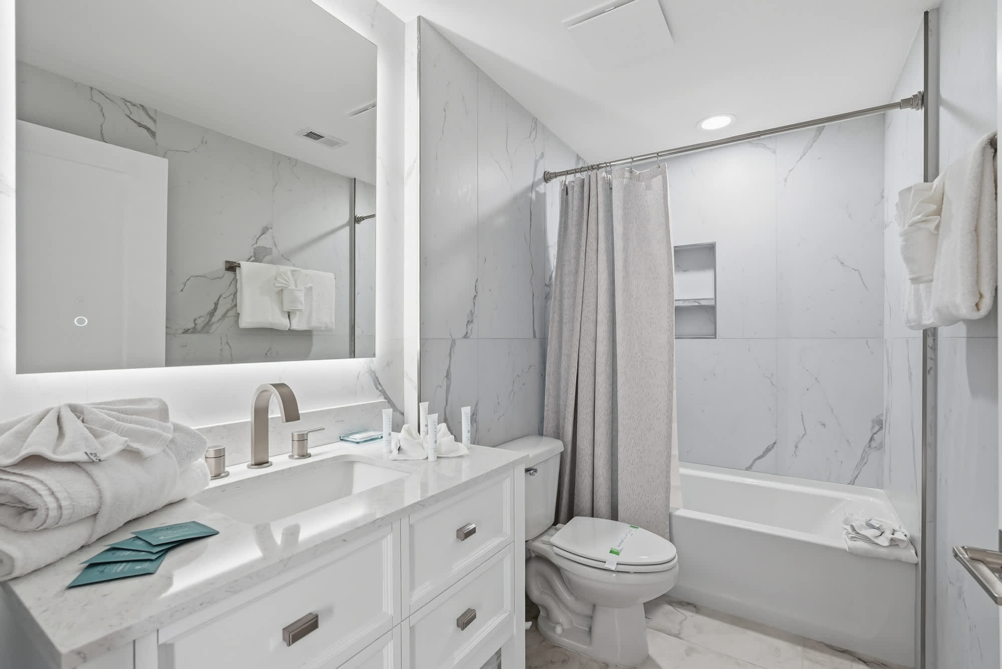 Tidewater 200 – Modern bathroom with marble walls, large mirror, white cabinetry, shower curtain, and bathtub.