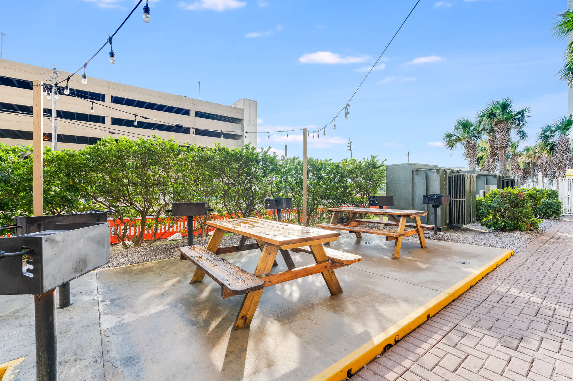 Tidewater 200 – Outdoor grilling area with picnic tables, surrounded by greenery and a view of a parking structure.
