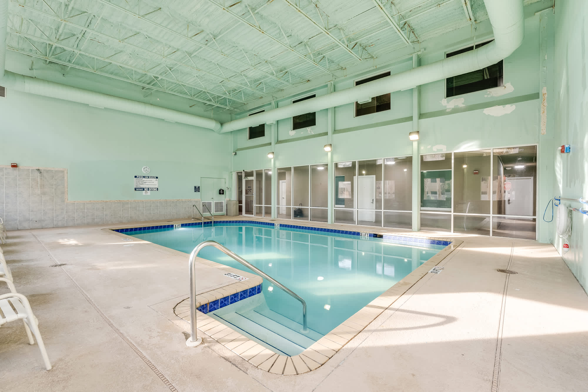 Tidewater 200 – Indoor pool area with turquoise walls, large windows, and seating along the sides.