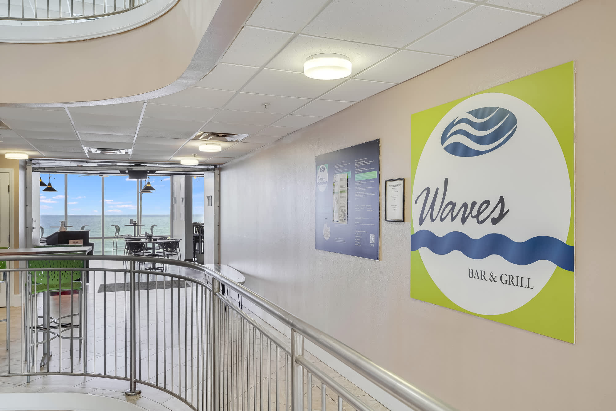 Tidewater 200 – Interior hallway with a sign for Waves Bar & Grill, ocean view visible through large windows.