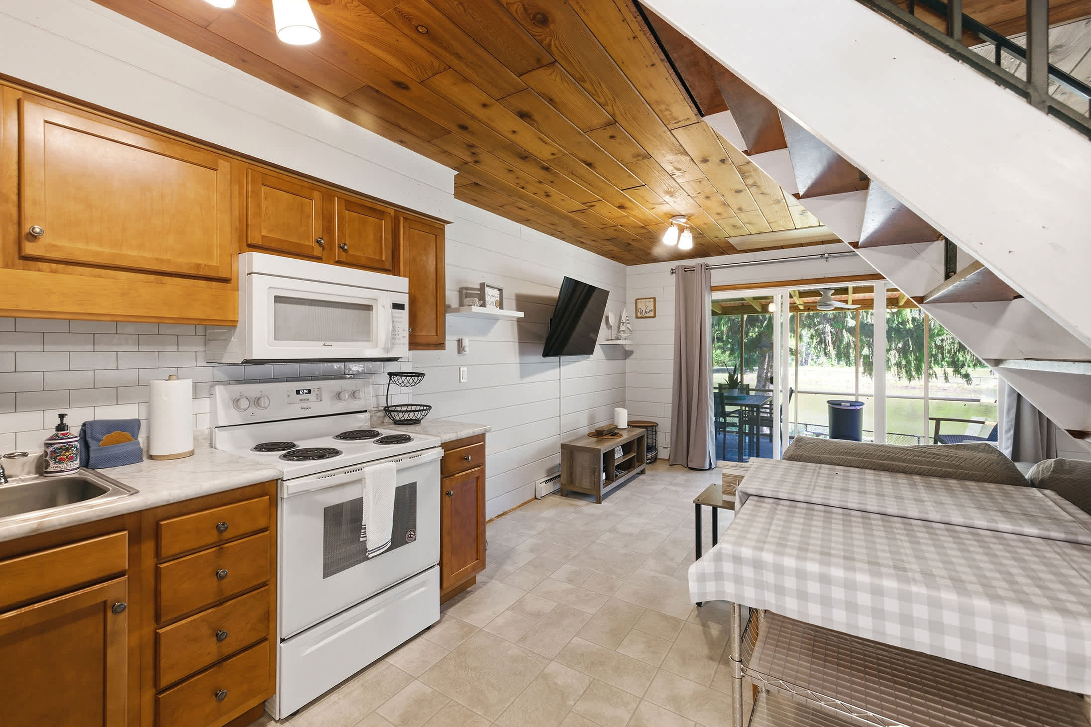 Open-plan kitchen and dining area with full appliances, TV, and direct access to the screened porch for easy flow between cooking, eating, and outside.