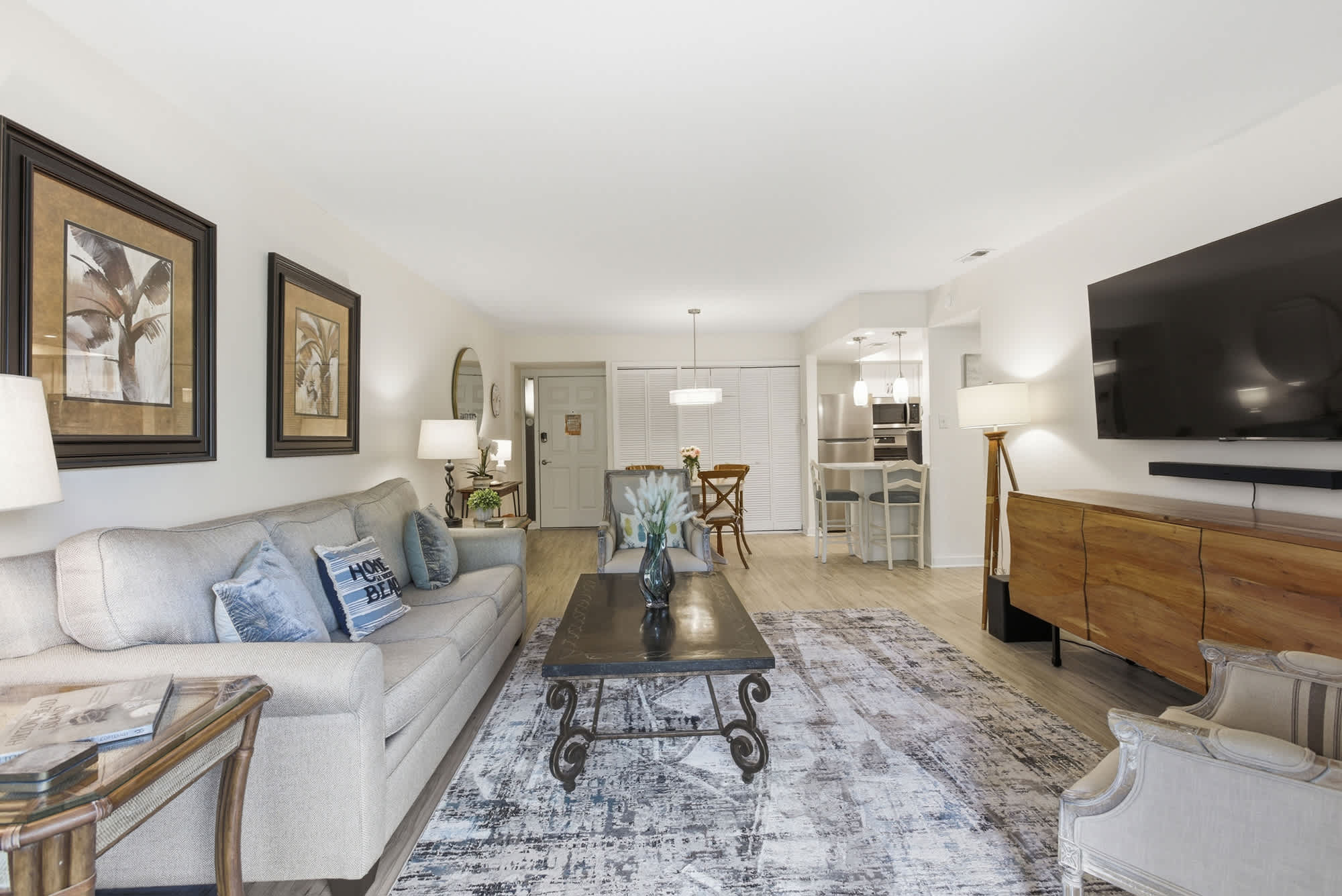 Woven textures and sea-blue accents ground this airy living room, where glowing lamps and rich wood grains create a soft, inviting ambiance. The open layout flows seamlessly, offering a spacious yet cozy spot to gather for a movie night.
