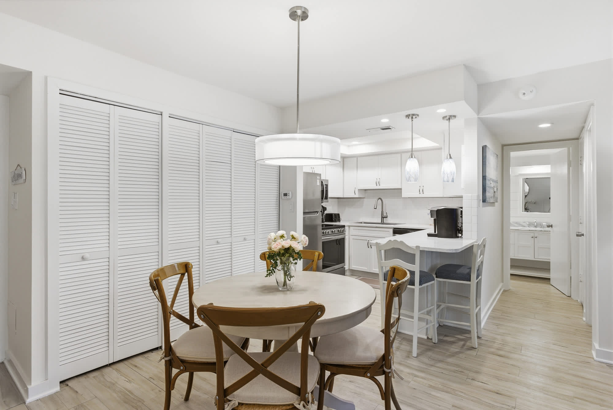 Honey-toned wood chairs surround a circular dining table, creating an intimate nook for morning coffee. Bright white finishes and soft pendant lighting give this open kitchen a clean, airy feel that invites slow breakfasts and easy conversation.