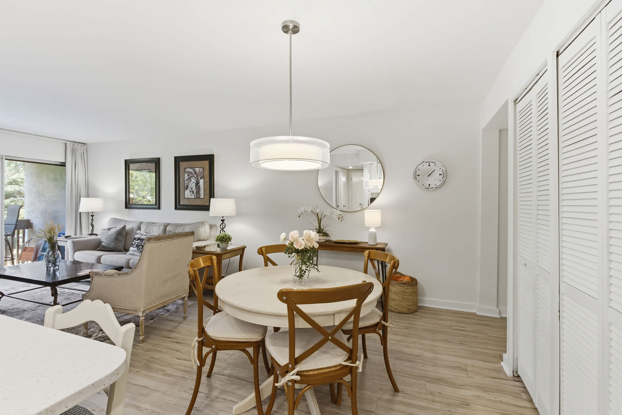 Pale wood floors and an airy open layout create a serene setting for morning coffee or casual dinners. Soft glow from the drum pendant illuminates the elegant round table, making every meal feel like a special occasion in this bright coastal home.