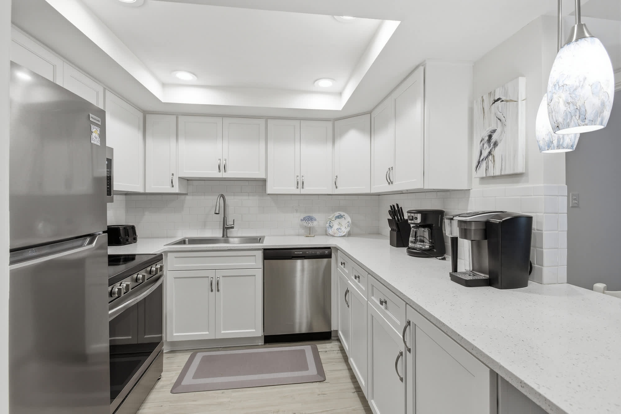 Stone counters and sleek stainless appliances sparkle under soft, recessed lighting in this airy kitchen. Artful pendant lamps and subway tiles create a bright, contemporary space perfectly prepared for your morning coffee and coastal meals.