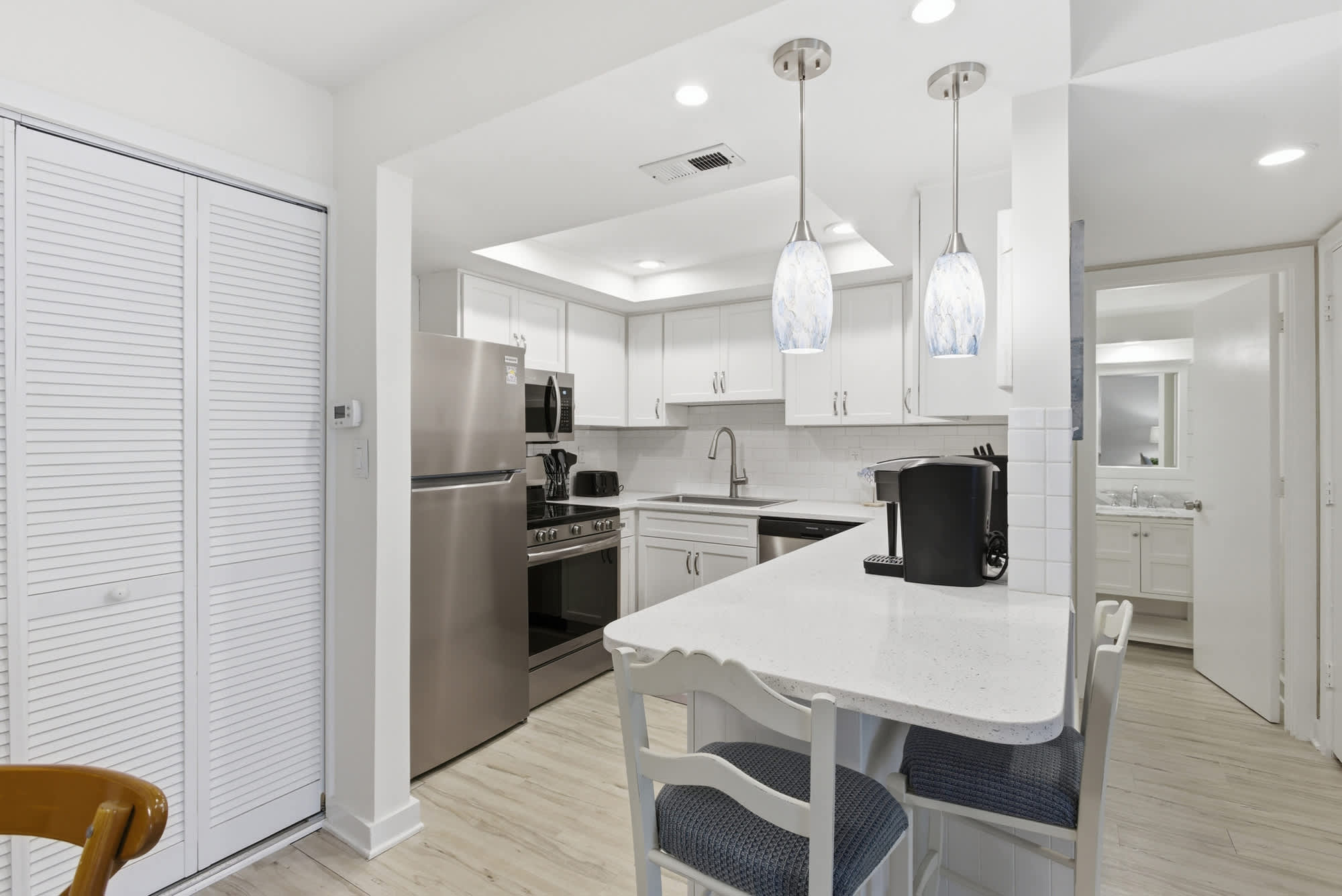 White quartz counters and sleek stainless appliances sparkle under artistic pendant lights, creating a bright and airy culinary corner. This modern kitchen offers a seamless flow for brewing morning coffee or prepping a sunset dinner.
