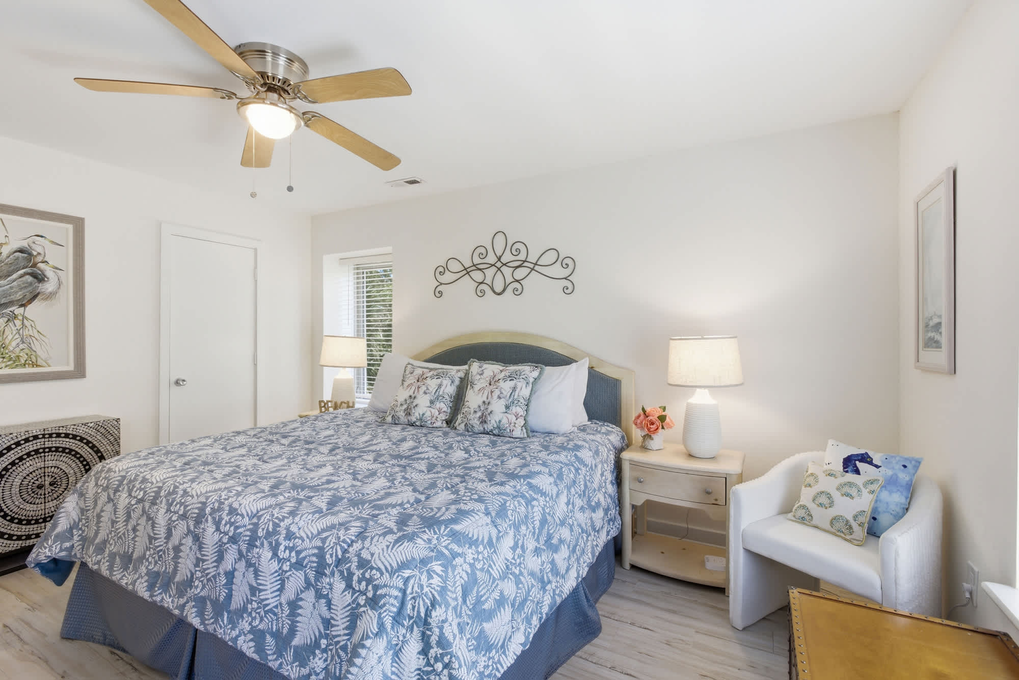 Indigo botanical patterns and soft bedside lamps create a calming atmosphere for a quiet night in. Natural wood textures from the ceiling fan and side tables anchor this airy bedroom, offering a serene space to rest.