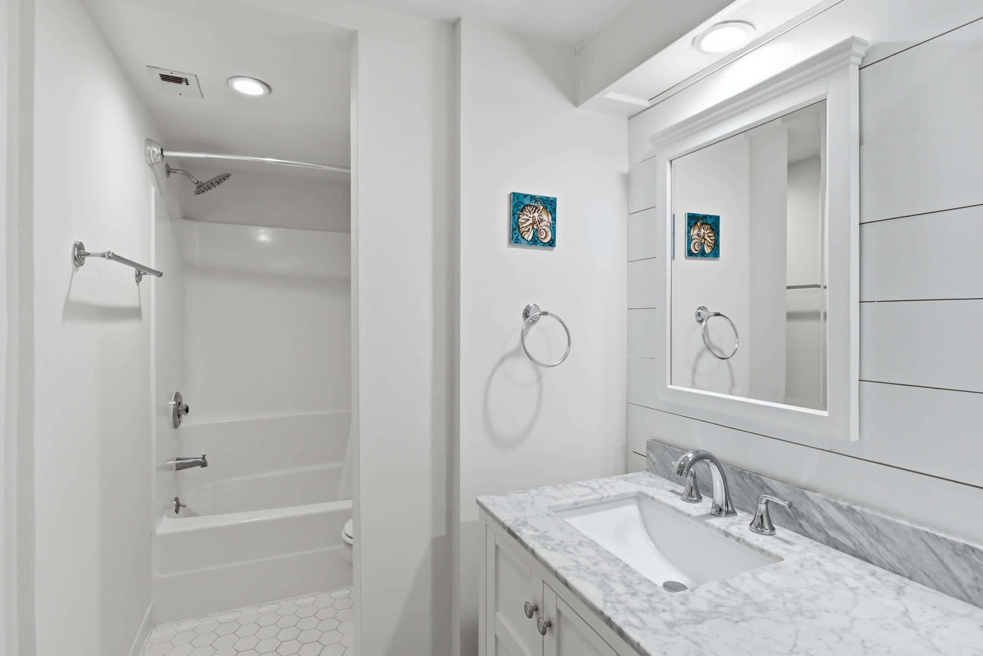 Marble surfaces and bright shiplap walls create a refreshing morning atmosphere in this clean, modern bathroom. Chrome fixtures gleam under steady light, while a deep soaking tub offers a quiet corner for your daily routine.