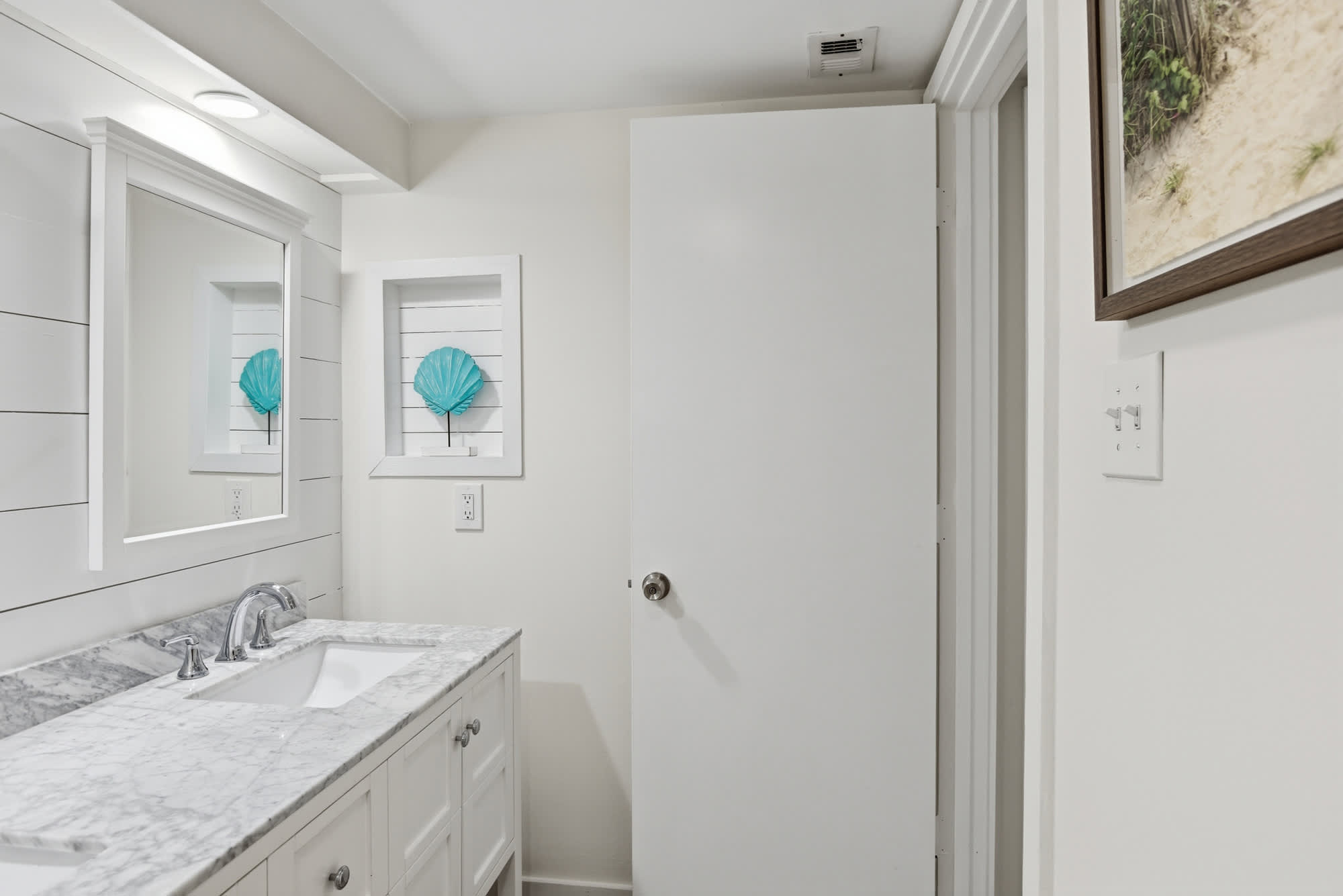 Shiplap walls and a cool turquoise shell bring a splash of coastal charm to this bright vanity area. Smooth grey veined surfaces and chrome fixtures sparkle under the soft glow of the overhead lights.