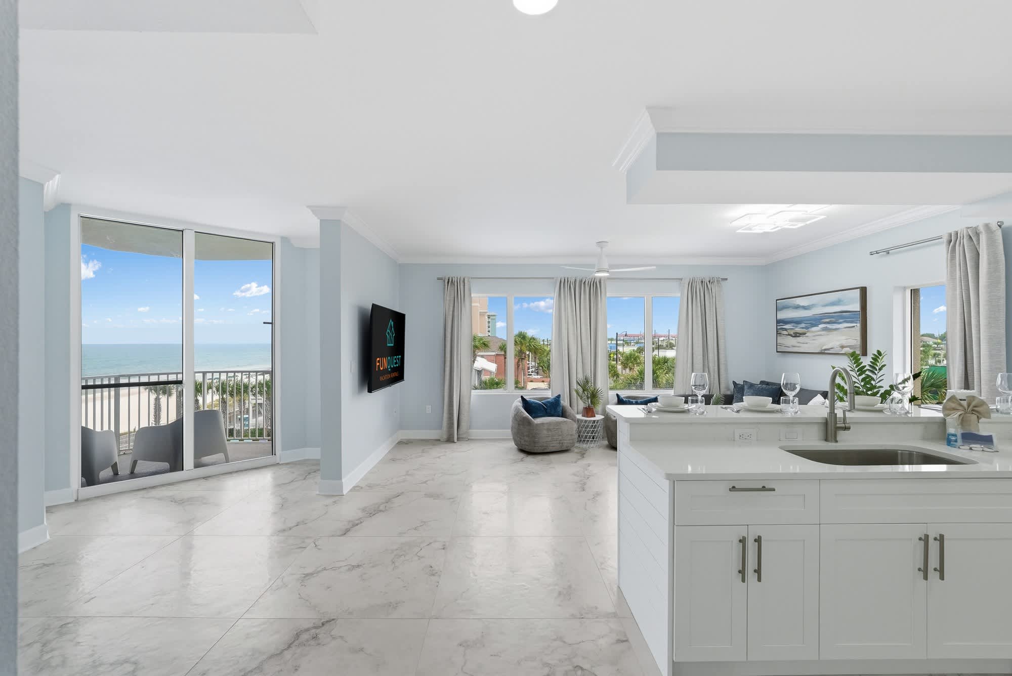 Tidewater 200 – Bright living area with ocean view, gray furniture, large windows, and a kitchen island.
