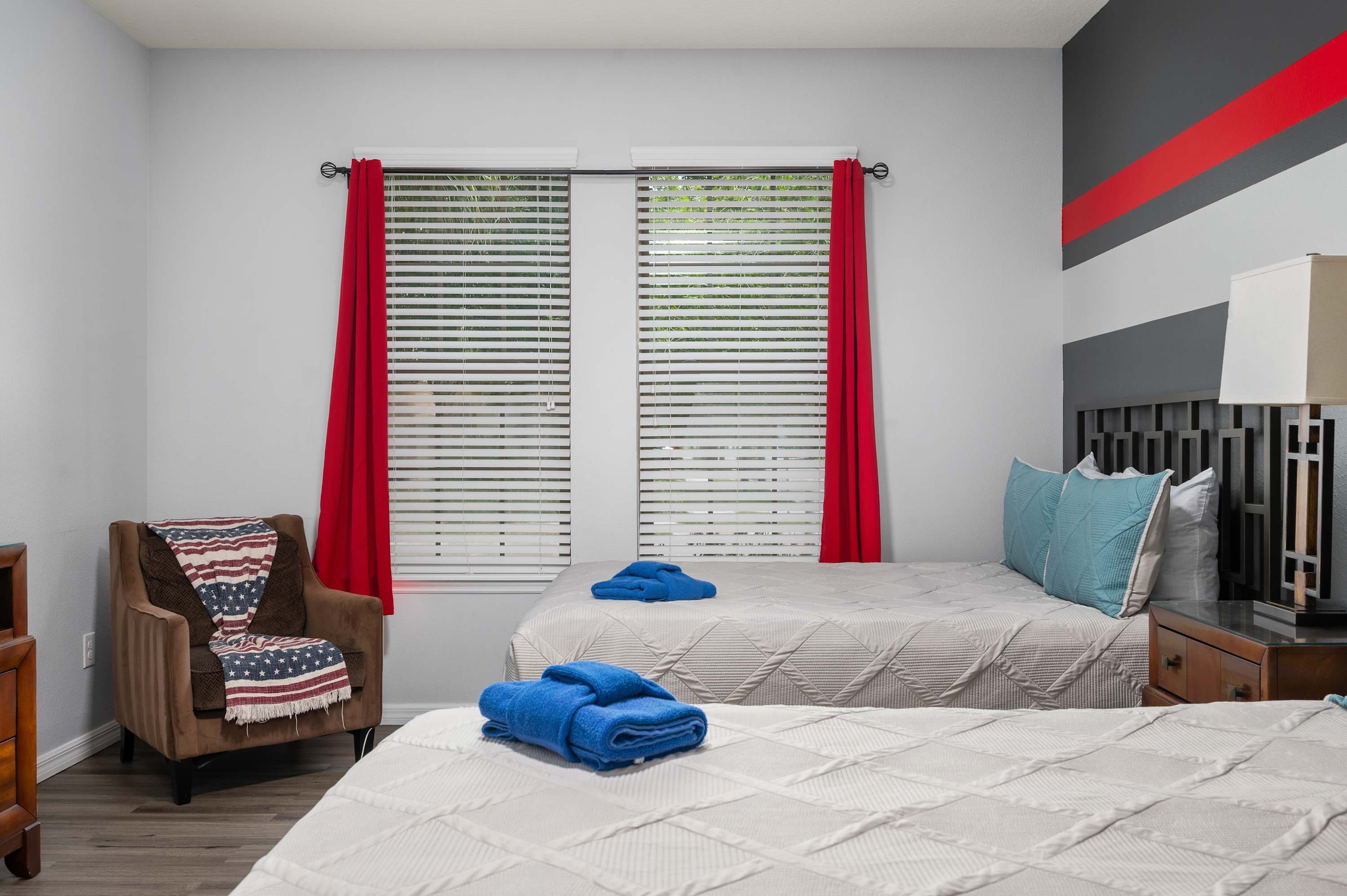 Cozy bedroom w/ two beds, red curtains & blue accent pillows — fun & welcoming.