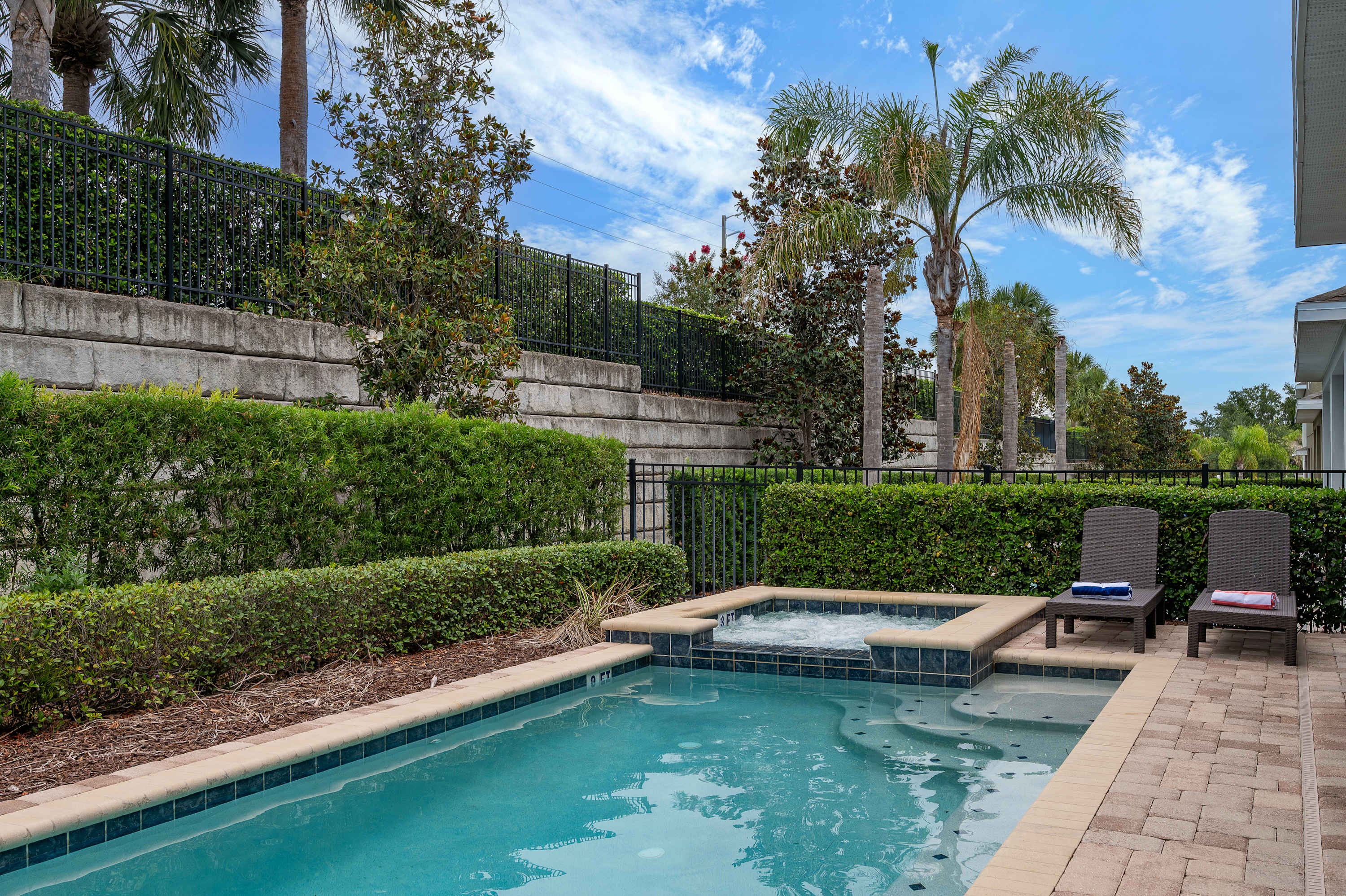 Relax by the pool and hot tub surrounded by lush greenery and palm trees.