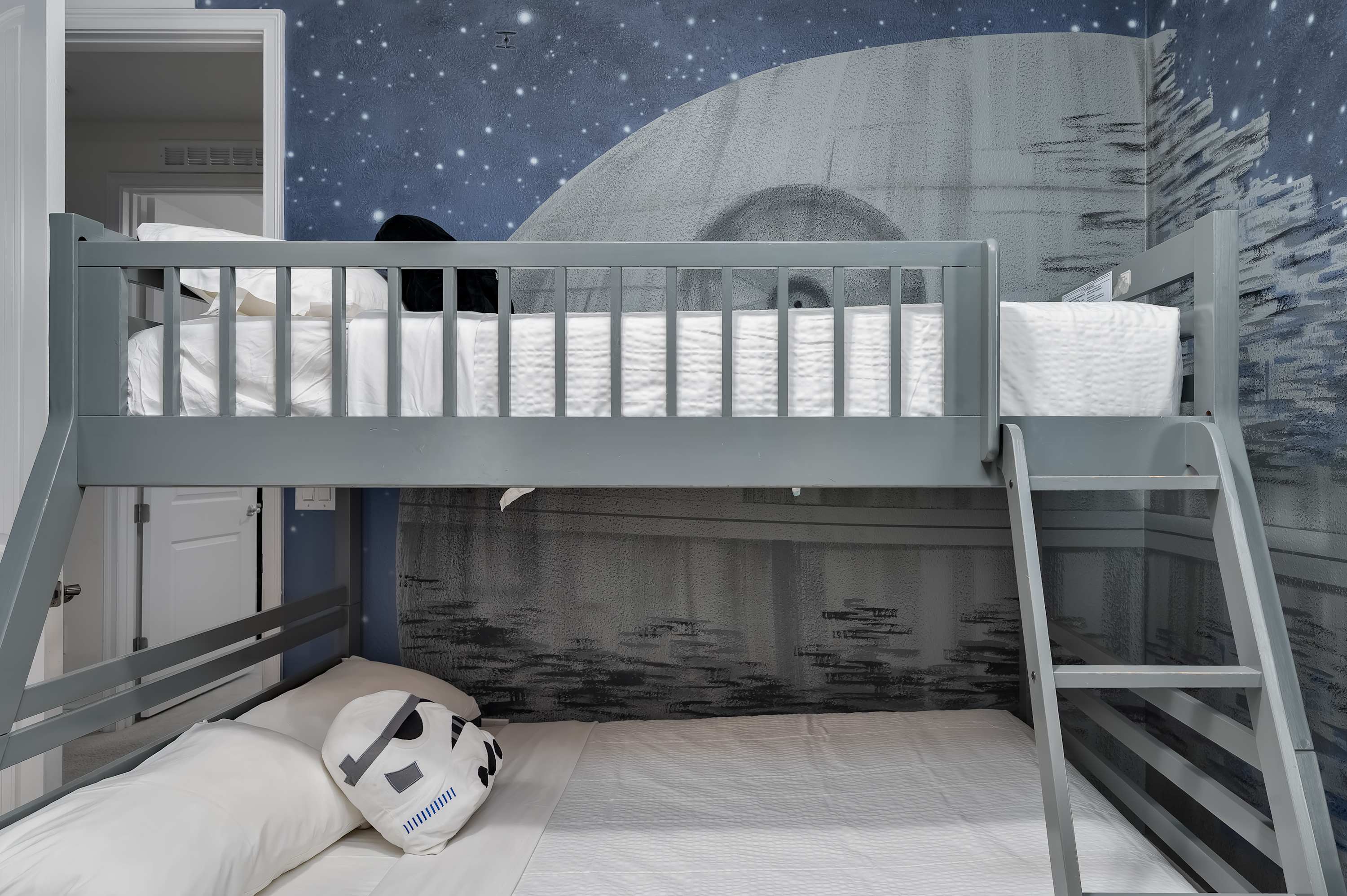 Gray bunk bed in a space-themed room with starry wall mural and stormtrooper pillow.