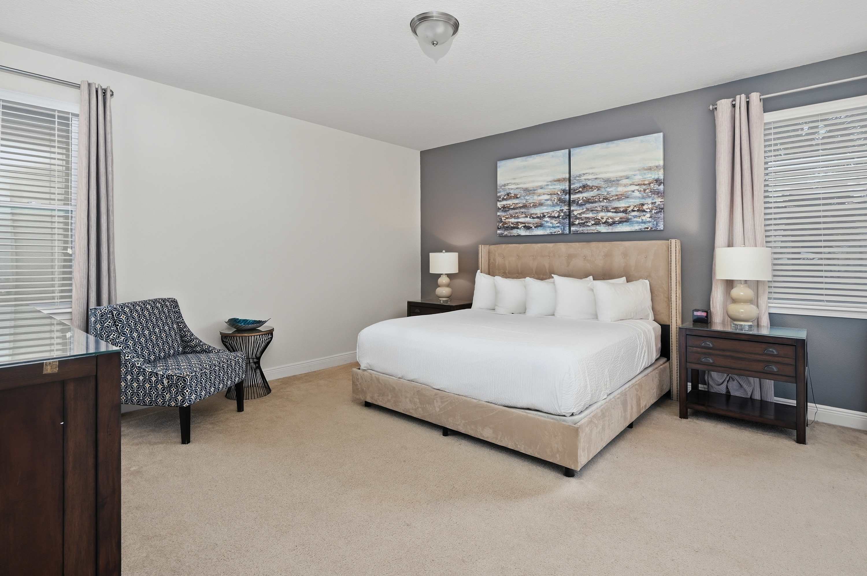 Spacious bedroom with a plush bed, modern artwork, and natural light from two windows.