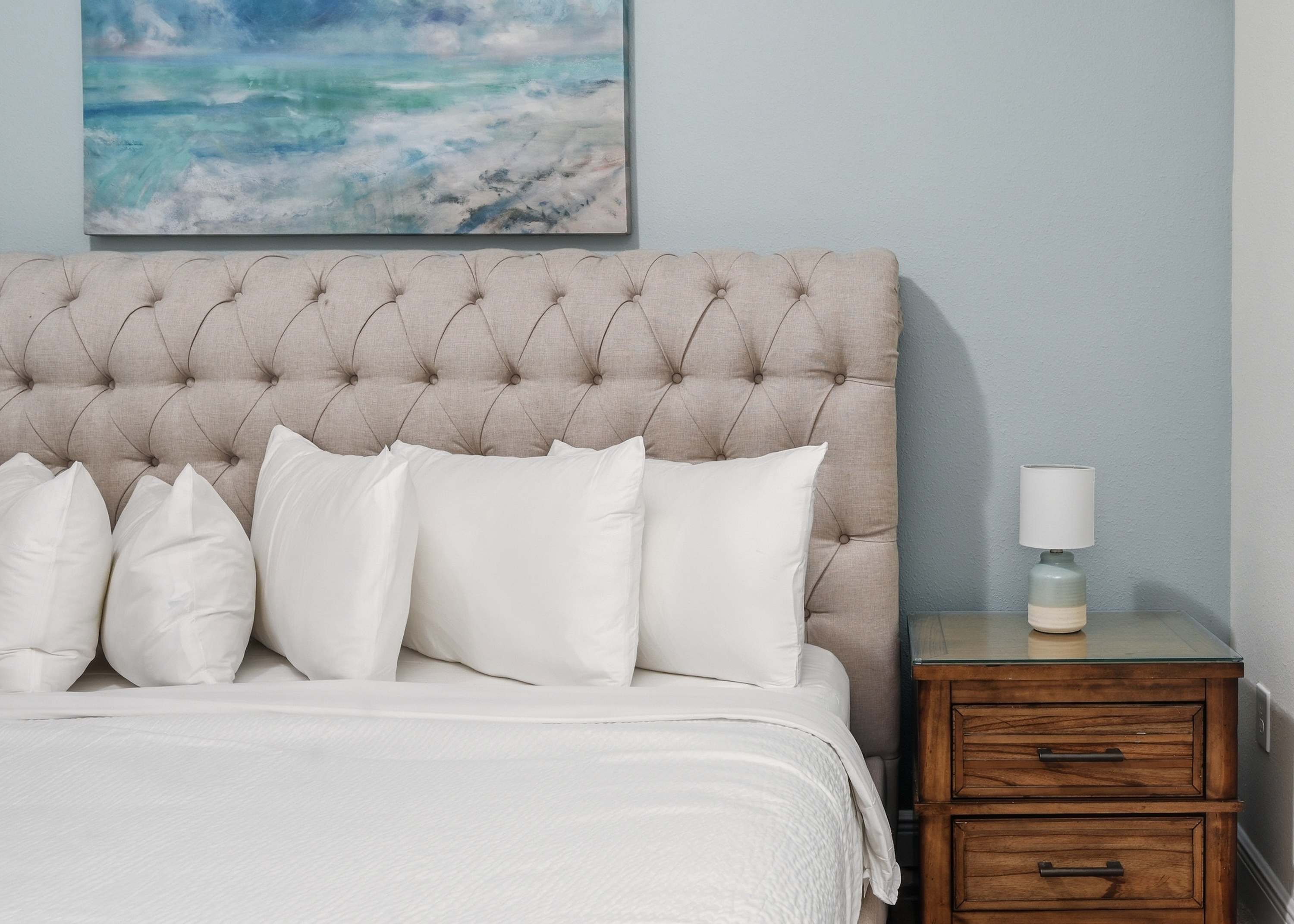 Comfortable bedroom with a tufted headboard and coastal artwork.