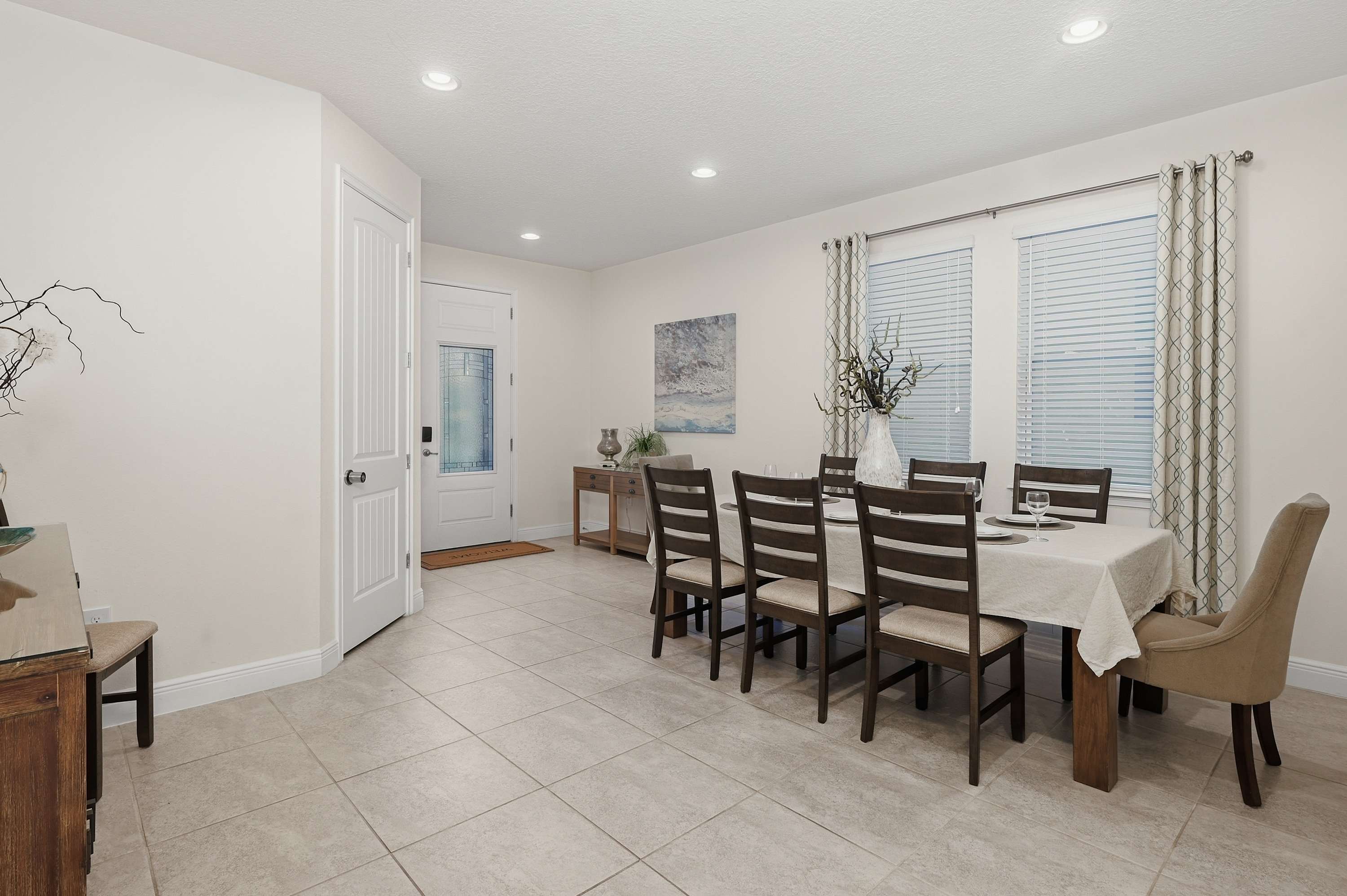 Dining area with a large table and natural light from windows with patterned curtains