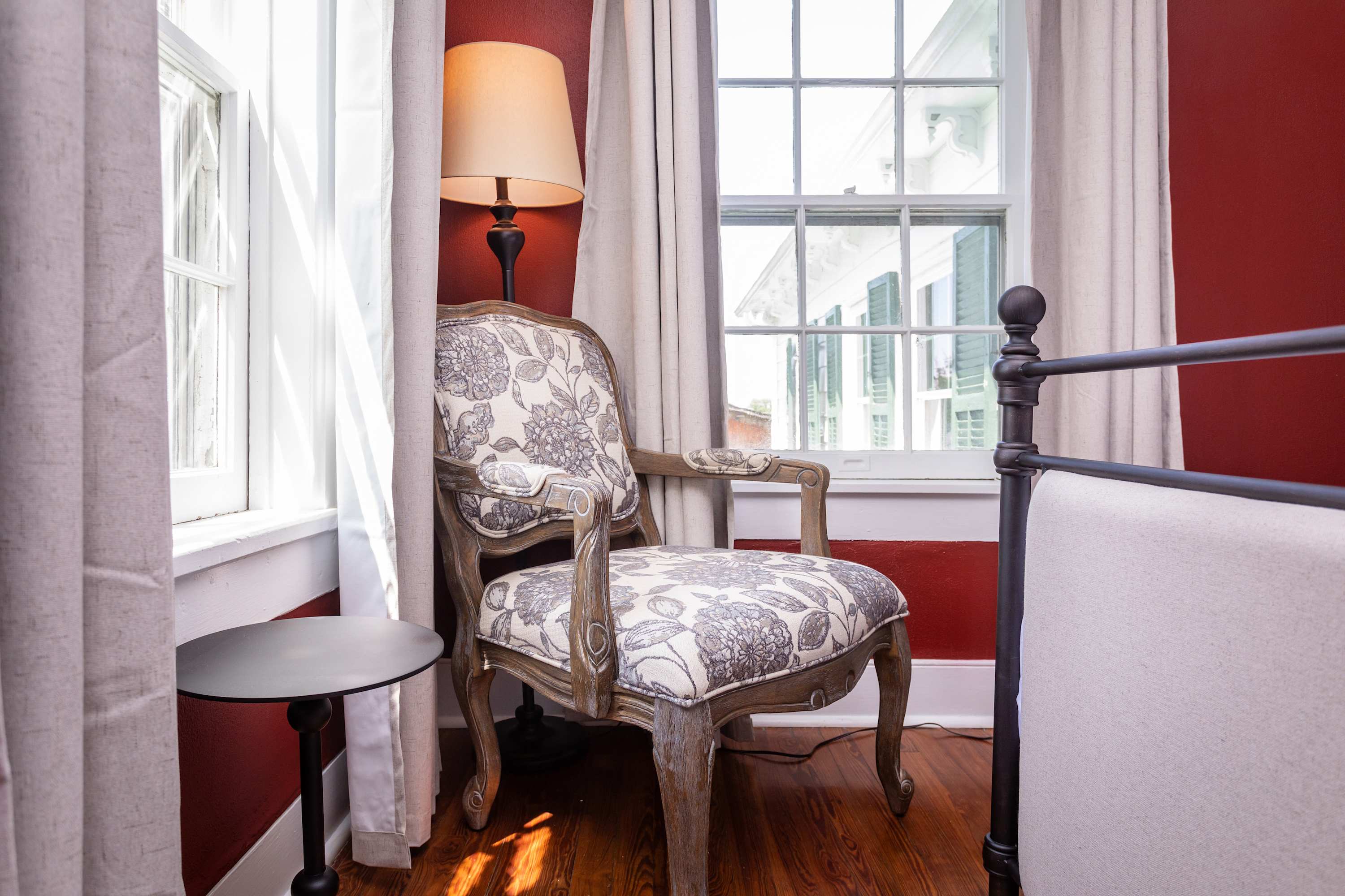 A cozy corner with a patterned armchair and natural light from large windows in a warmly painted room.