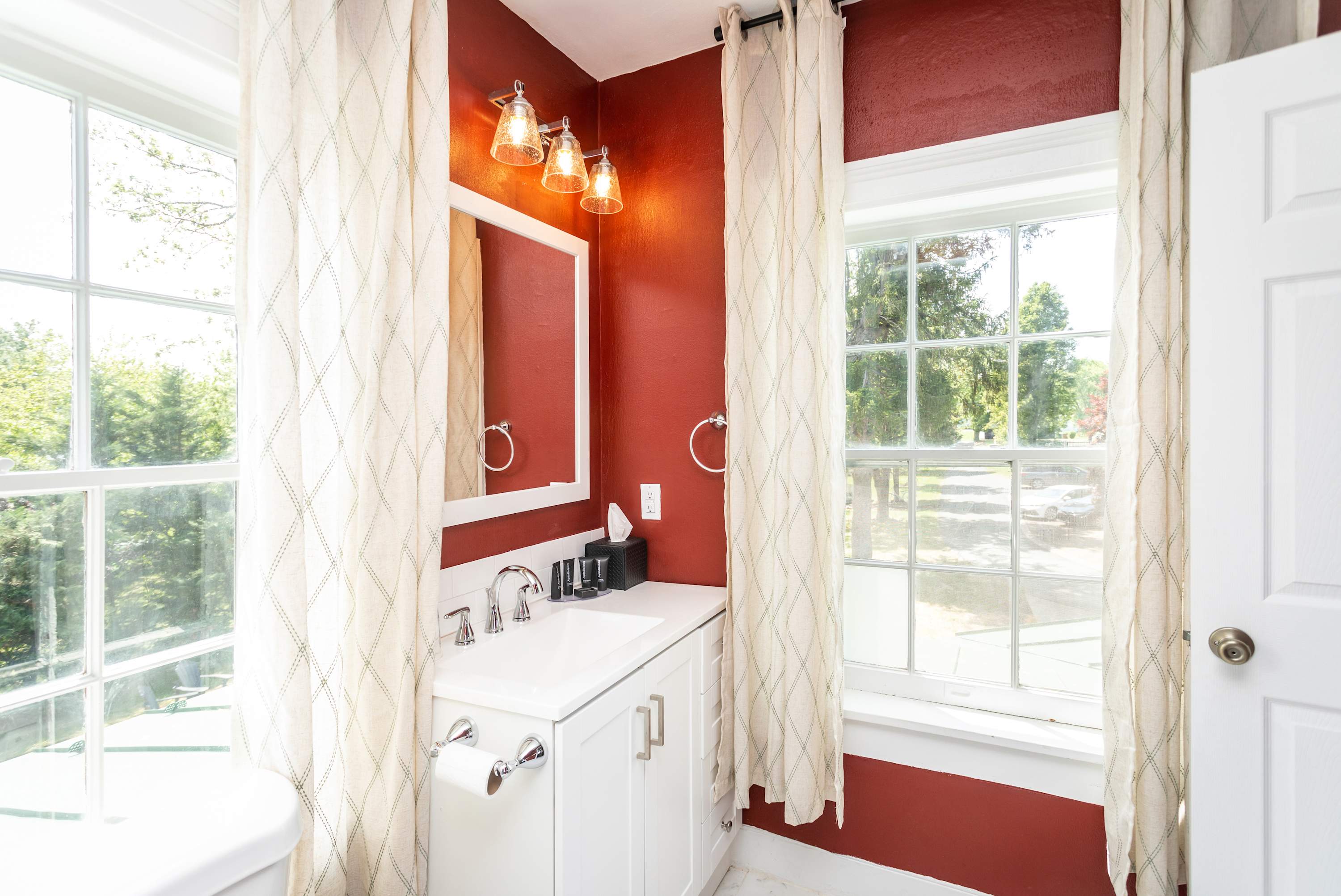Natural light fills this bathroom with red walls and white vanity for a bright, inviting space.