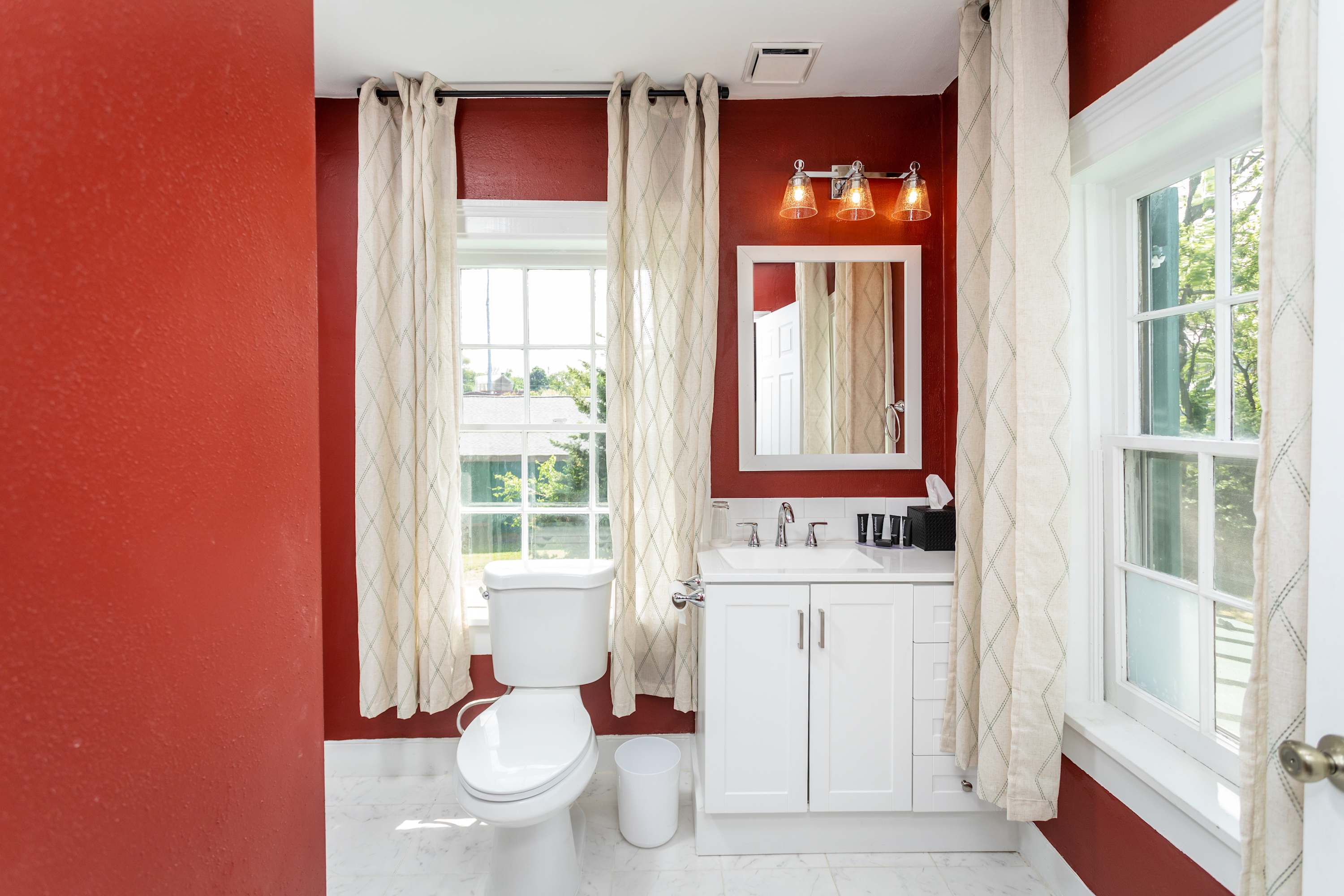 Bright bathroom with red walls, white vanity, and large windows for natural light