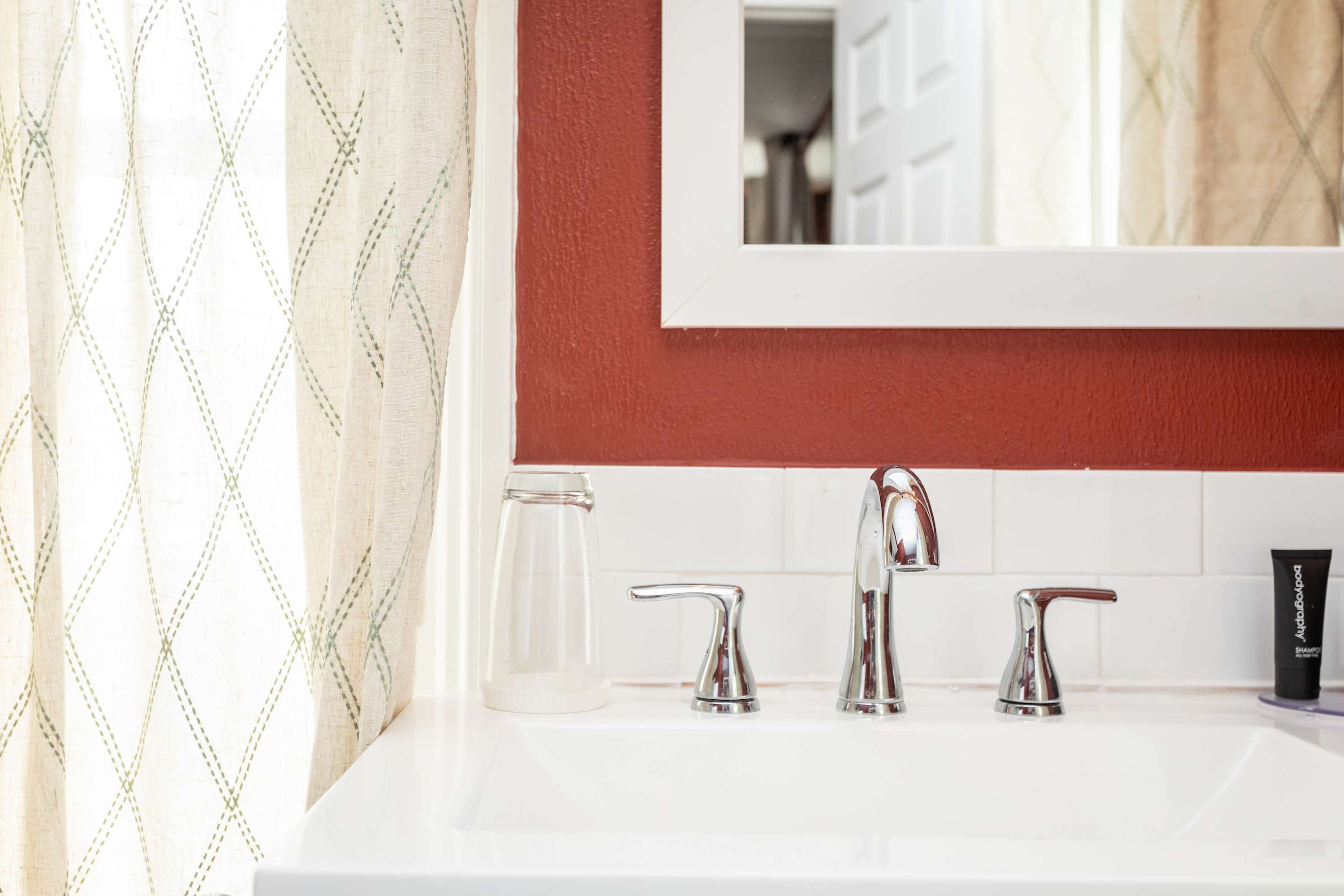 Modern bathroom sink with chrome fixtures and a white framed mirror against a red wall