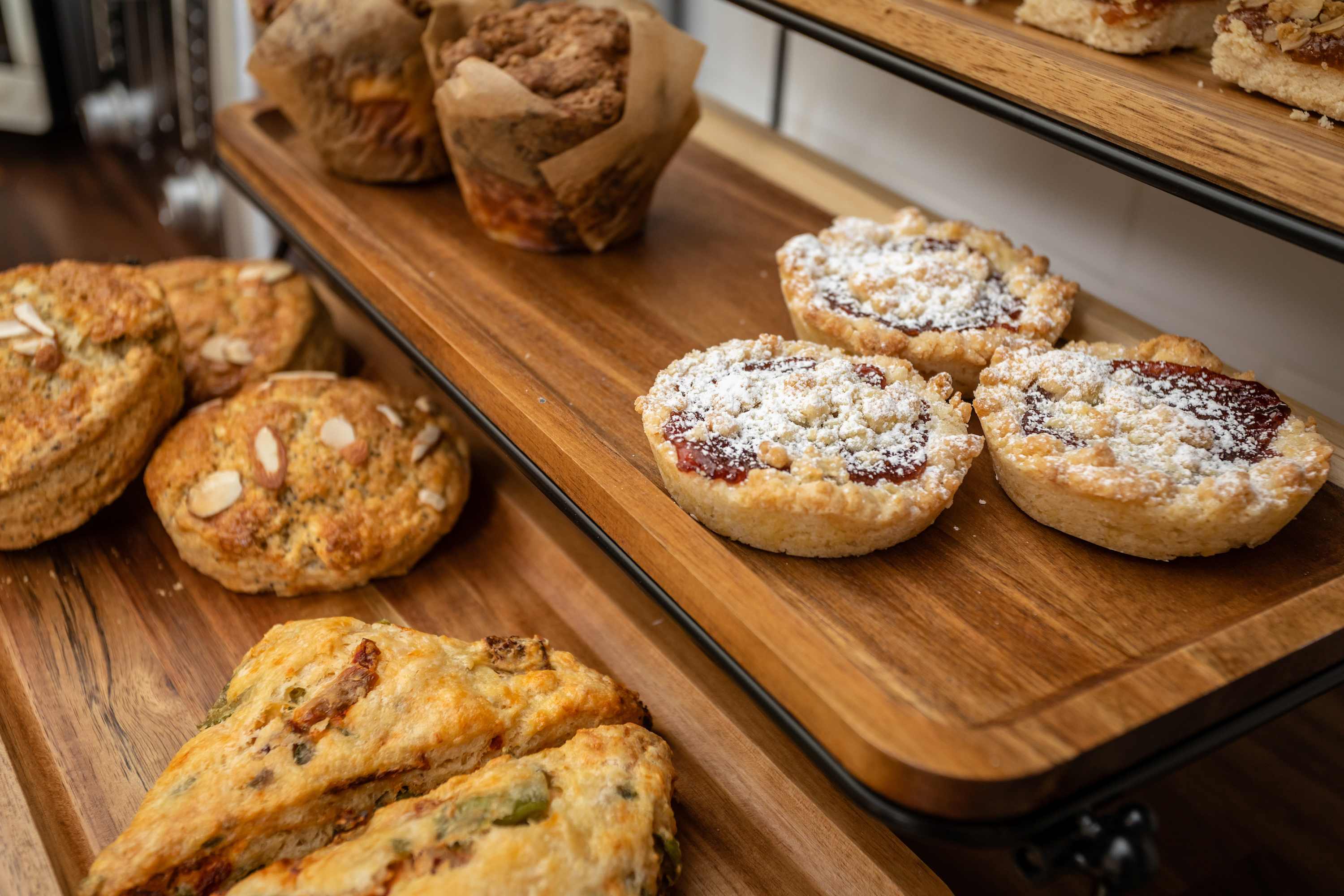 Freshly baked scones, muffins, and jam tarts displayed on wooden shelves for a cozy breakfast experience.